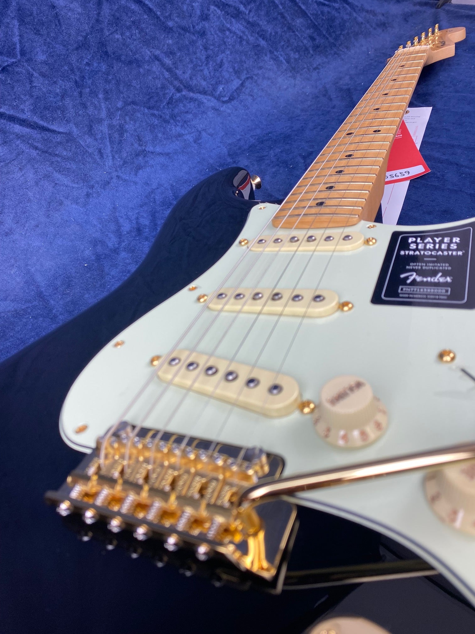 Close-up of a Fender Stratocaster electric guitar with gold bridge hardware, cream pickups, maple neck, and light green pickguard on a blue surface.