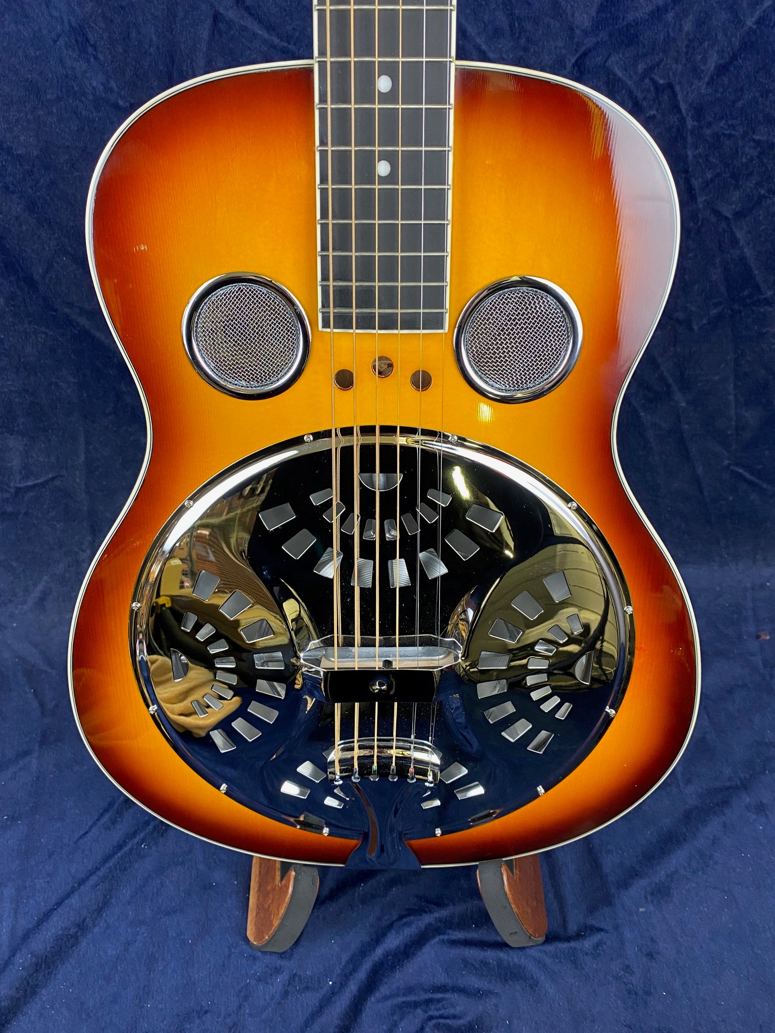 Sunburst finish resonator guitar with two round metal sound holes and a large, shiny, patterned metal cover plate in the lower body.