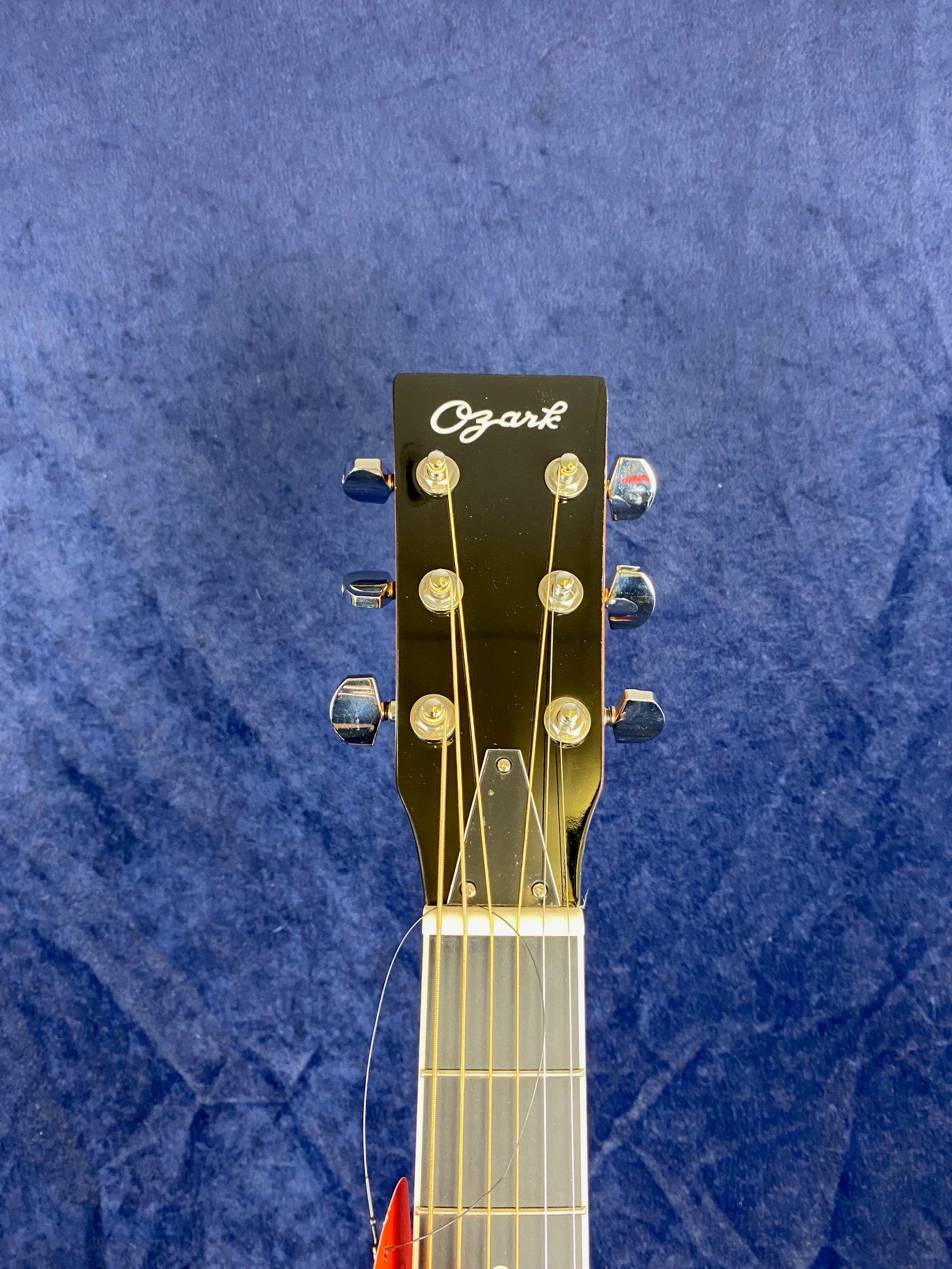 Black Ozark resonator headstock with six metal tuning pegs and six strings against a textured blue background.