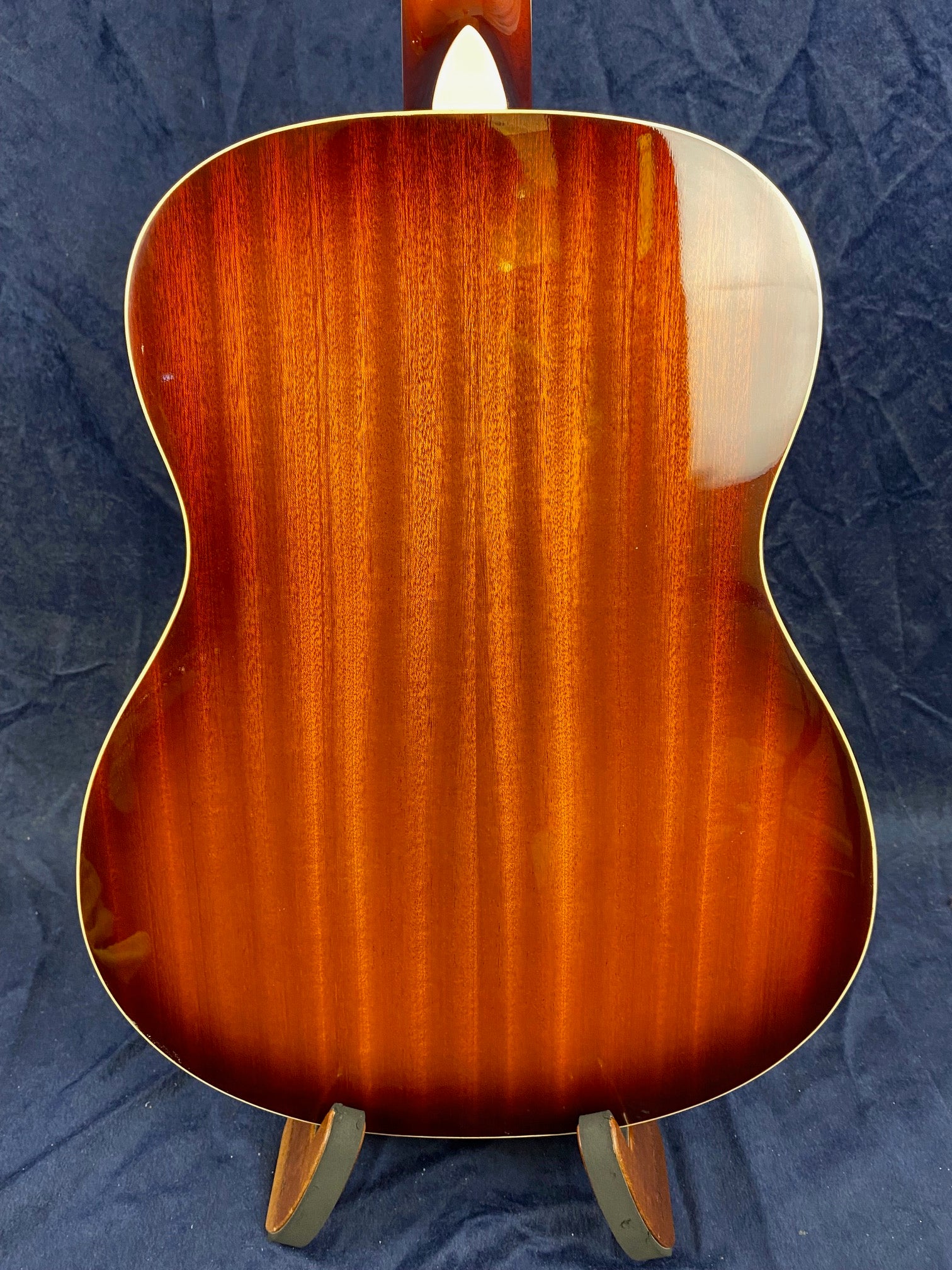 Back view of a resonator guitar with a glossy, reddish-brown wood finish and subtle vertical grain patterns, displayed on a stand.