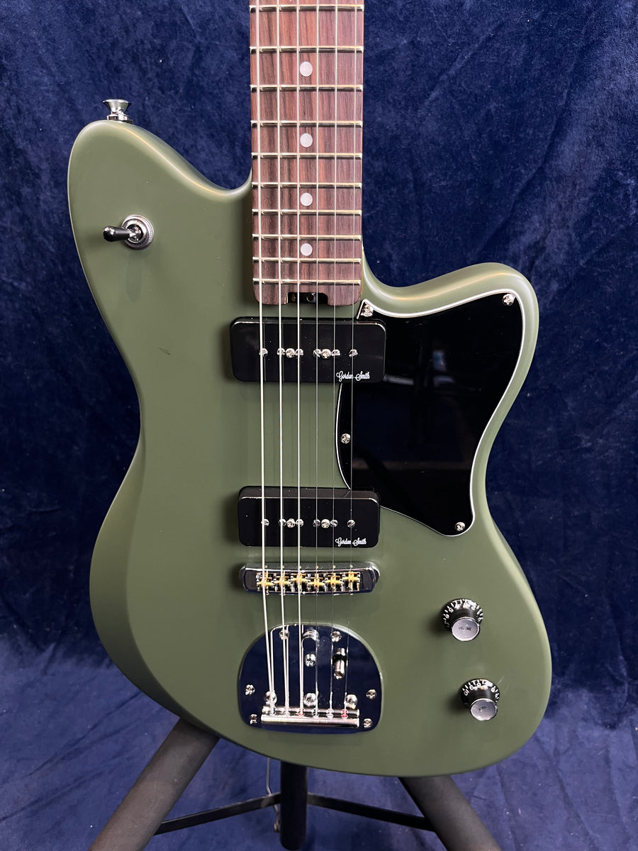 Olive green electric guitar with two black pickups, black pickguard, chrome hardware, two control knobs, and a toggle switch on the upper horn.