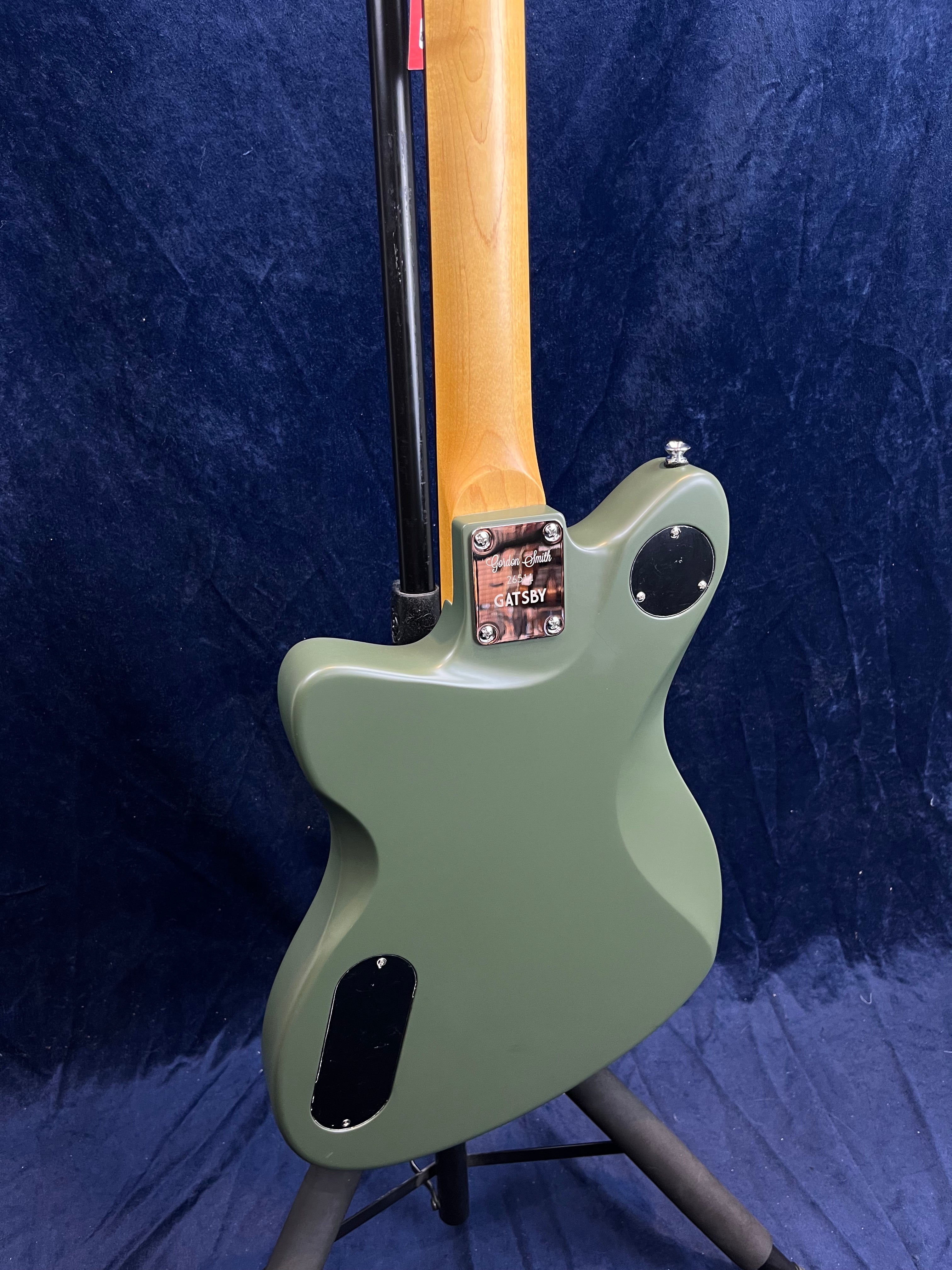 Green electric guitar viewed from the back, showing a natural wood neck and two black covers on the body with a metal neck plate labeled "Gatsby."