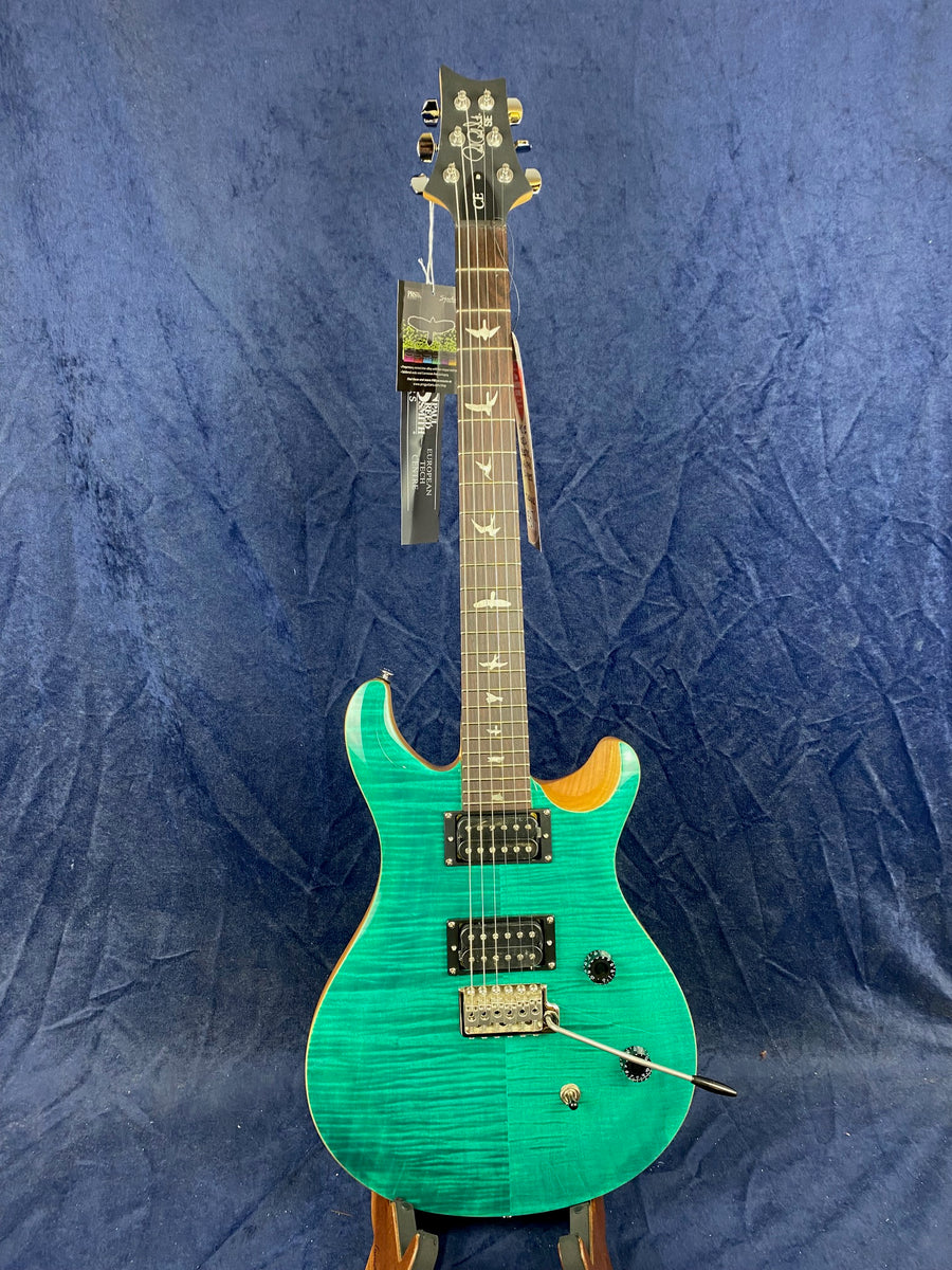 A teal electric guitar with two humbucker pickups, bird inlays on the fretboard, black knobs, and a silver tremolo arm, displayed upright.