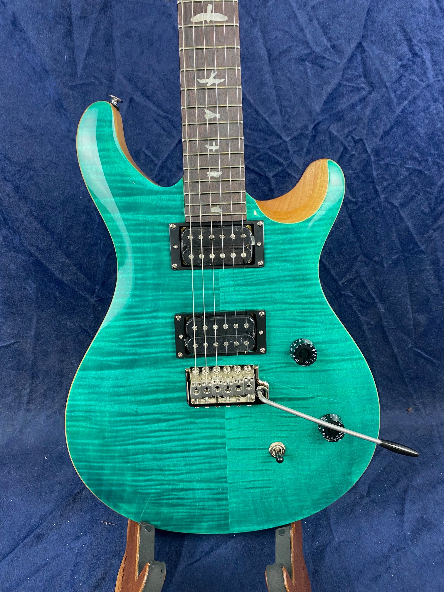 Turquoise electric guitar with wood grain, dual humbucker pickups, bird inlays on the fretboard, and a whammy bar.