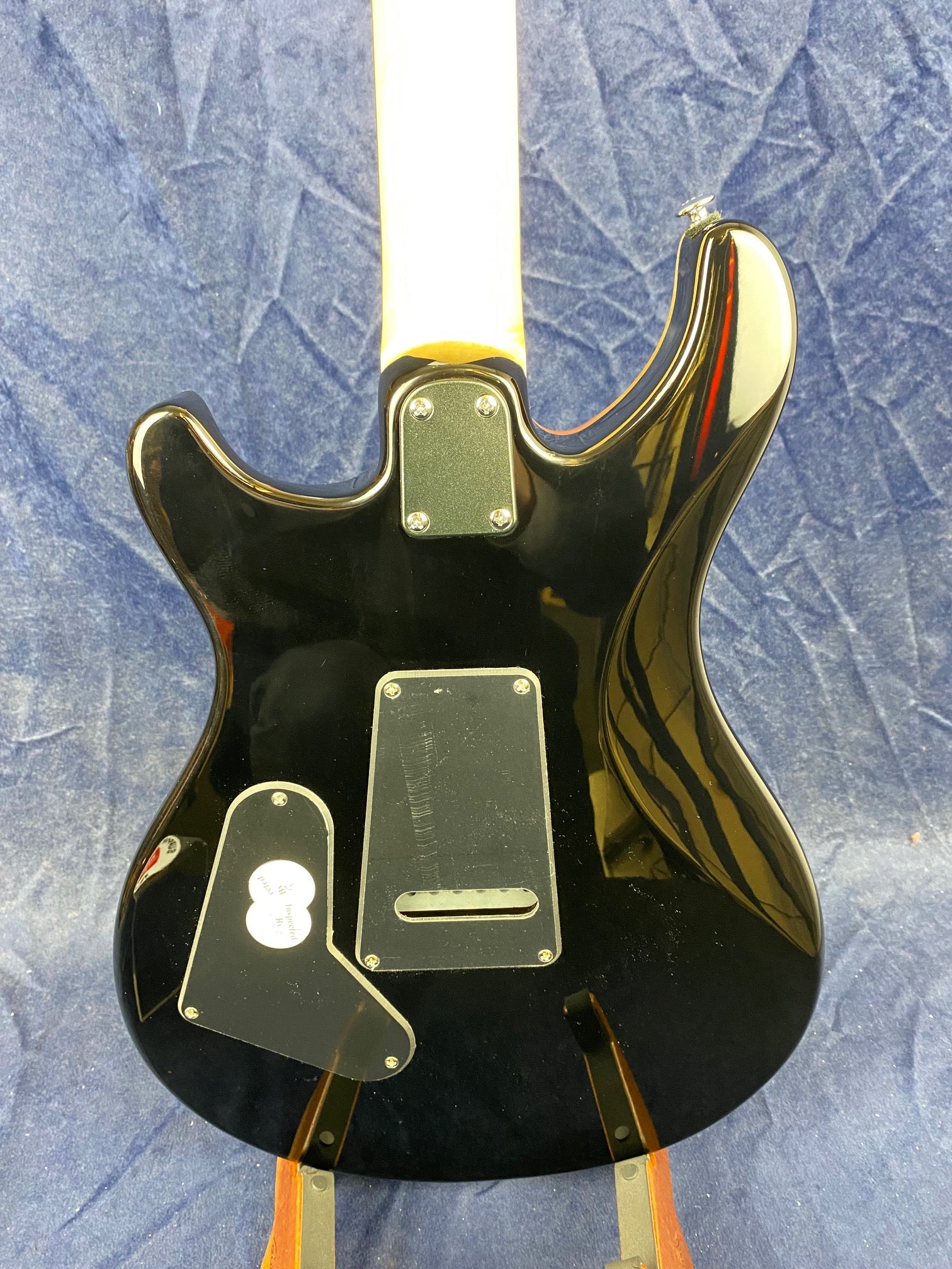 Black electric guitar seen from the back, showing two plastic access panels, a bolt-on neck, and a shiny finish reflecting light.