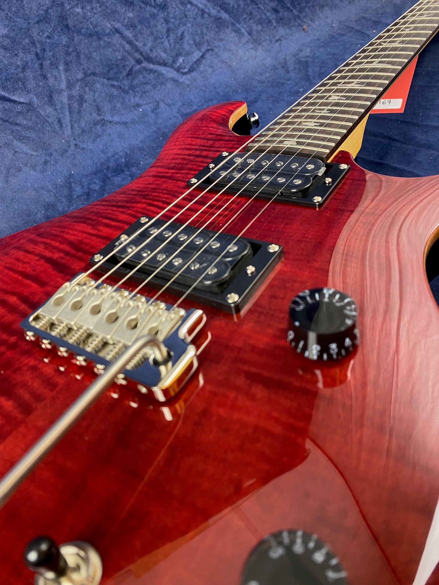 Electric guitar with a glossy red finish, two black humbucker pickups, tremolo bridge, and black control knobs on a dark blue fabric background.