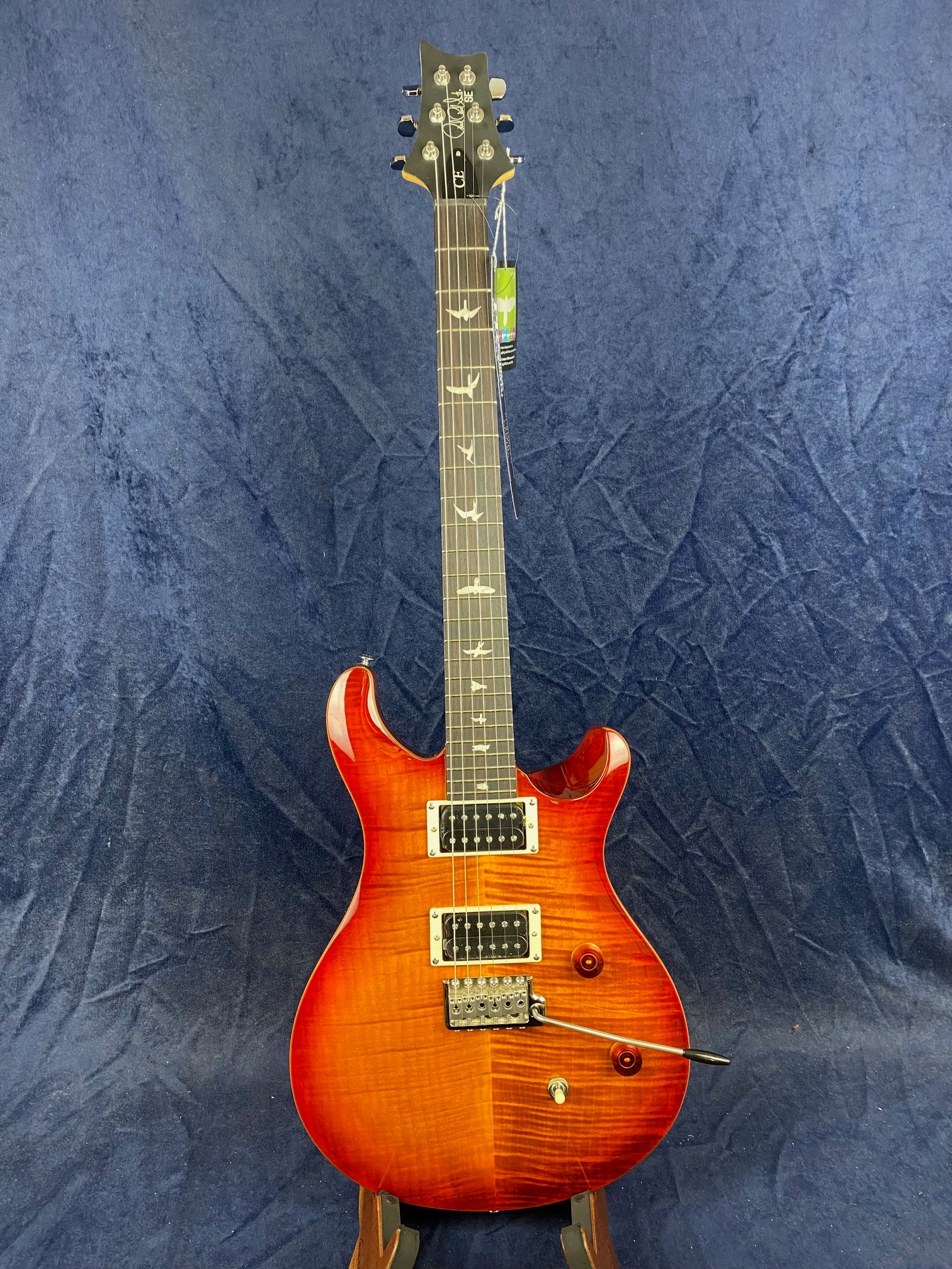 Electric guitar with a glossy sunburst red finish, two humbucker pickups, bird inlays on the fretboard, and a whammy bar, set against a blue background.