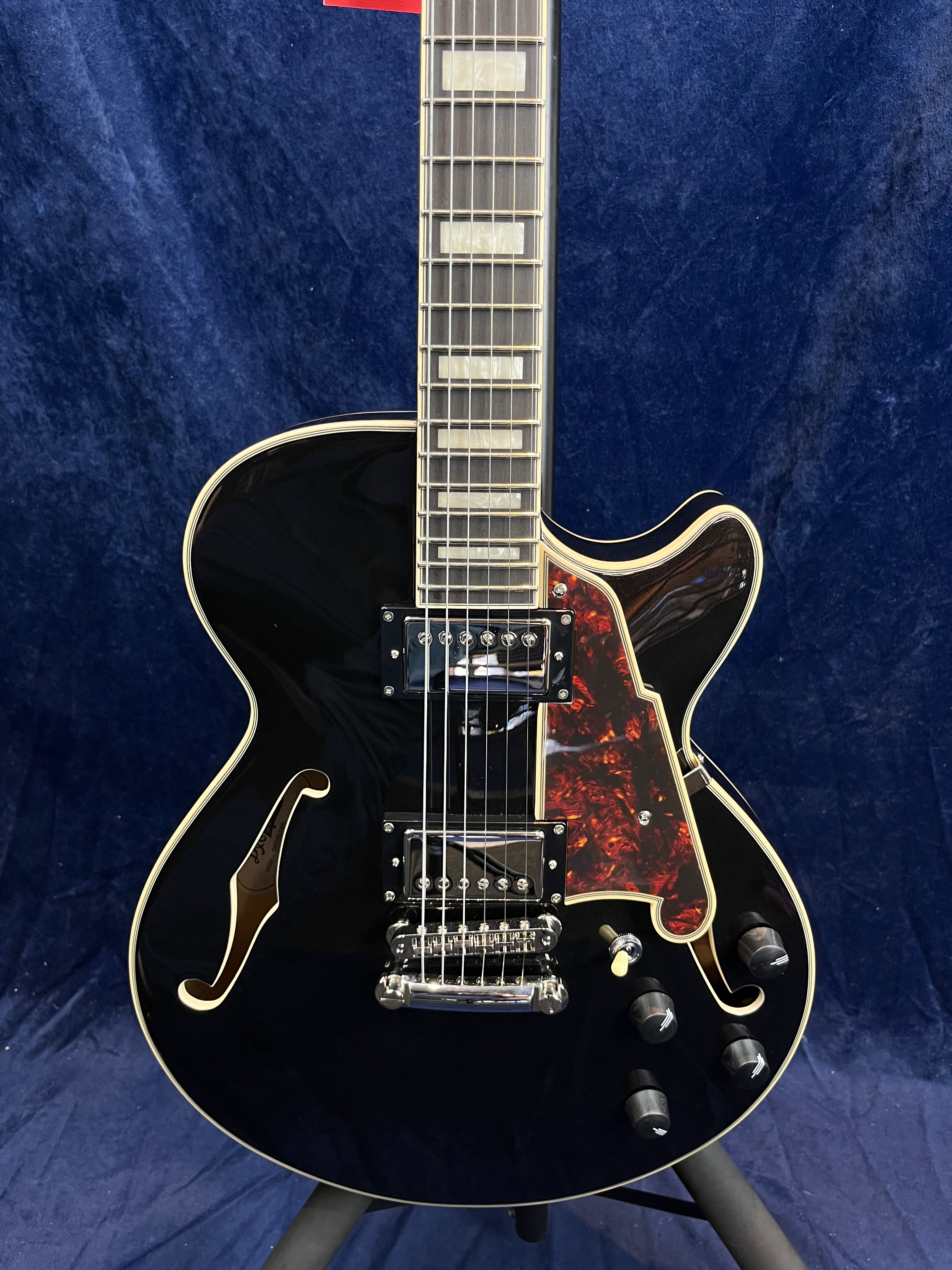Black semi-hollow electric guitar with double humbucker pickups, a tortoiseshell pickguard, gold-trimmed f-holes, and four black control knobs.