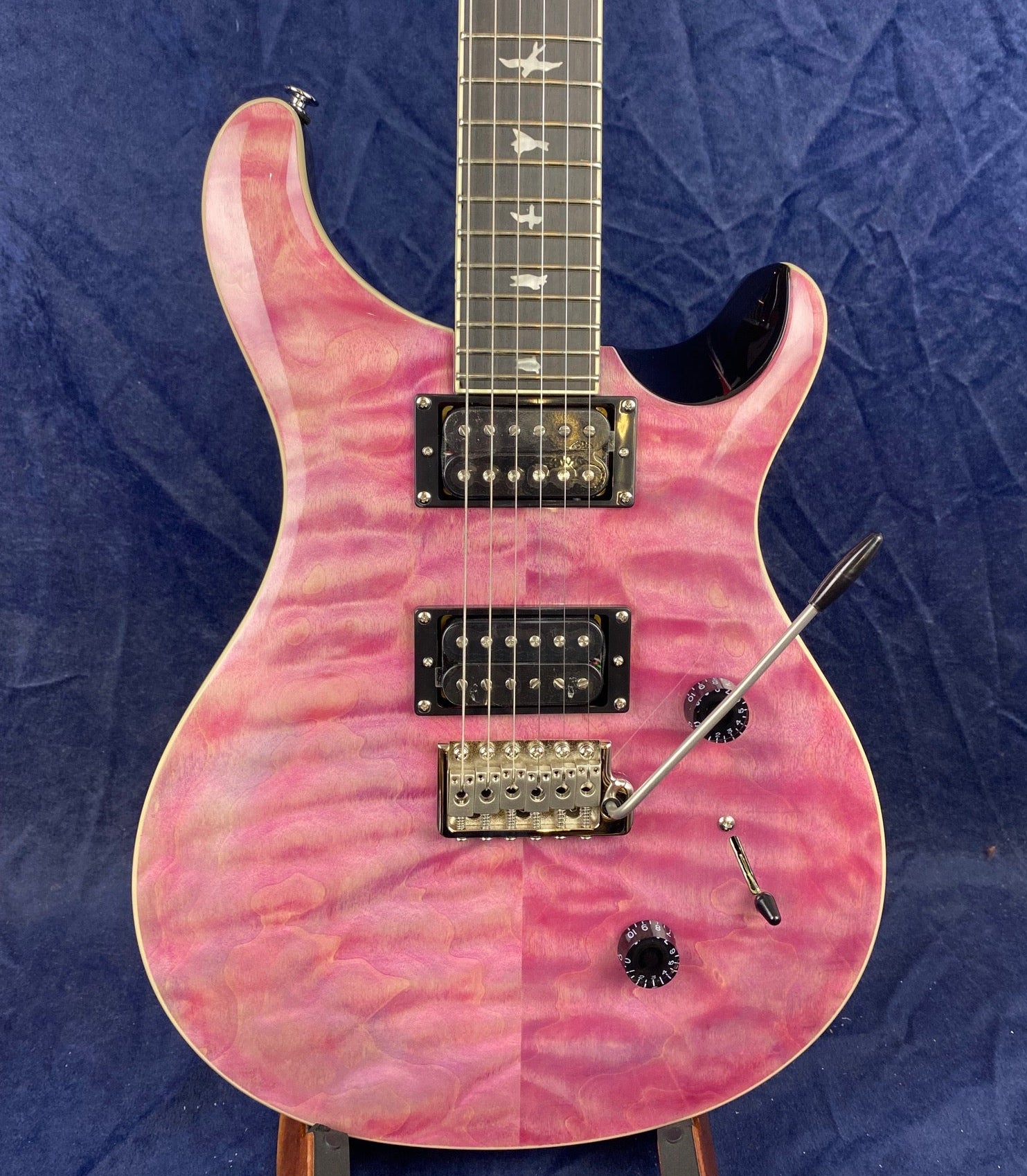 Pink electric guitar with a quilted maple top, two humbucker pickups, bird inlays on the fretboard, and a whammy bar.