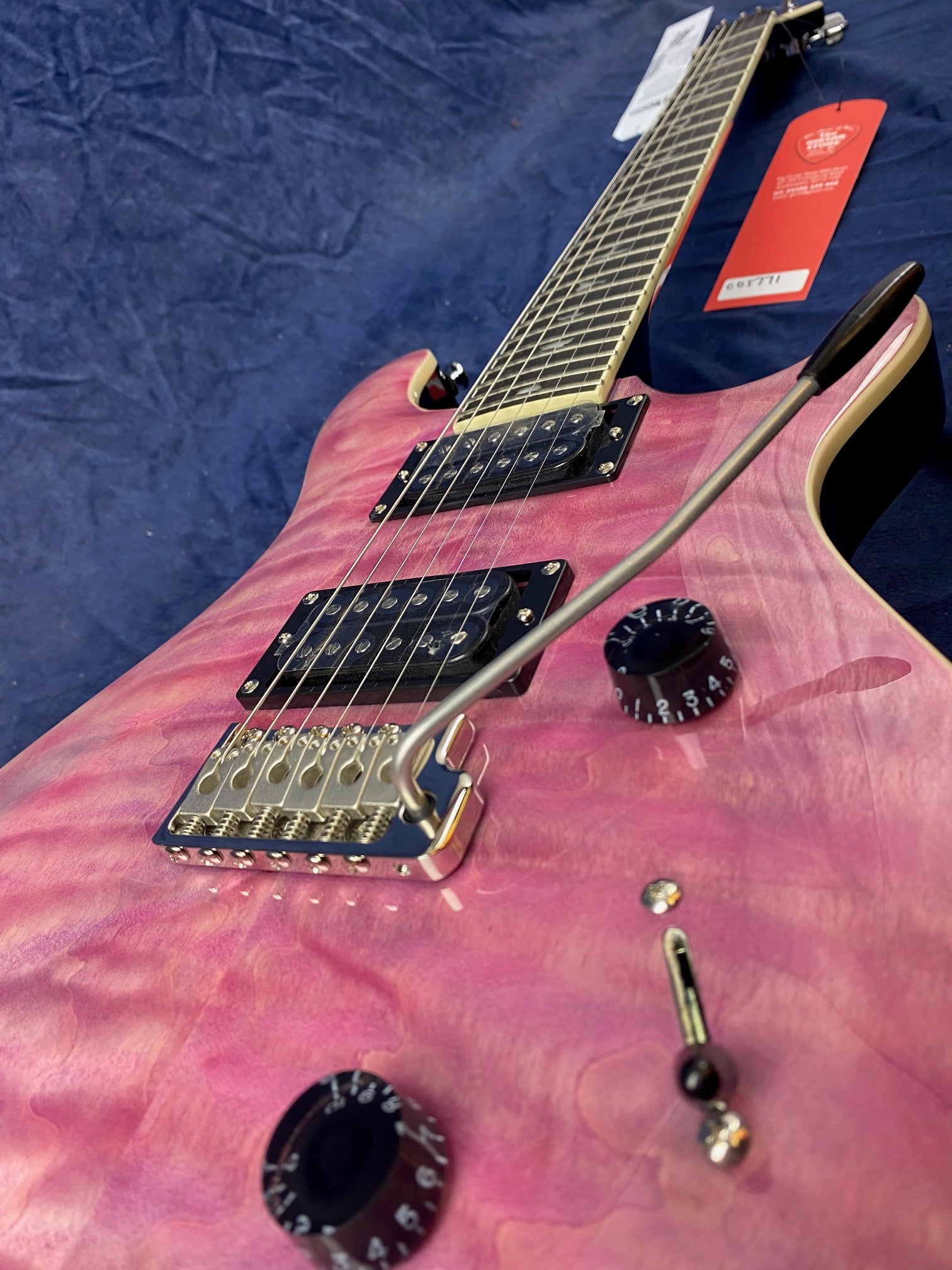 Electric guitar with a quilted pink finish, dual humbucker pickups, gold bridge, black control knobs, and a whammy bar. Tags attached to the headstock.