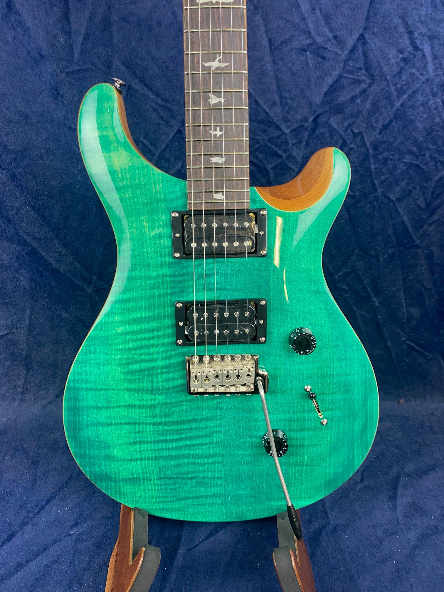 Green electric guitar with dual humbucker pickups, bird inlays on the fretboard, two control knobs, a tremolo bridge, and a three-way switch.