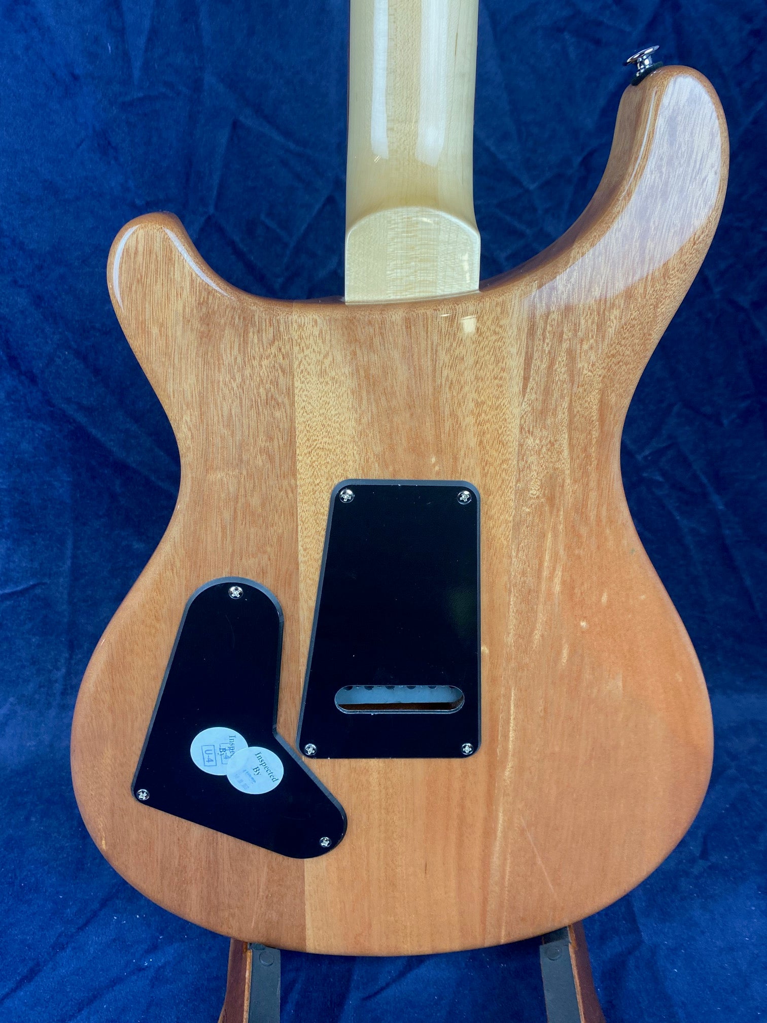 Natural wood finish electric guitar back, two black plastic covers attached with screws, light-colored neck, against a dark blue background.
