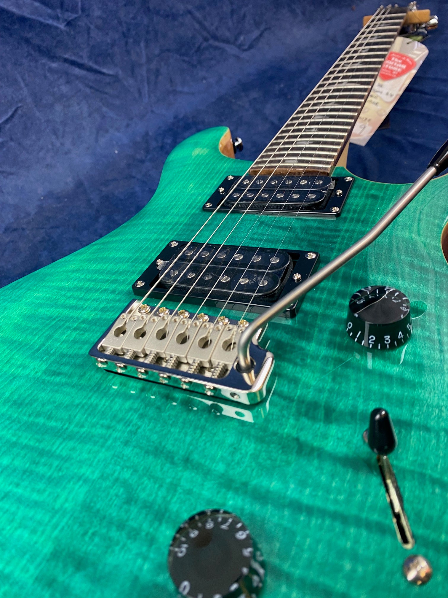 A green electric guitar with two humbucker pickups, a whammy bar, black control knobs, and a visible patterned wood grain finish.