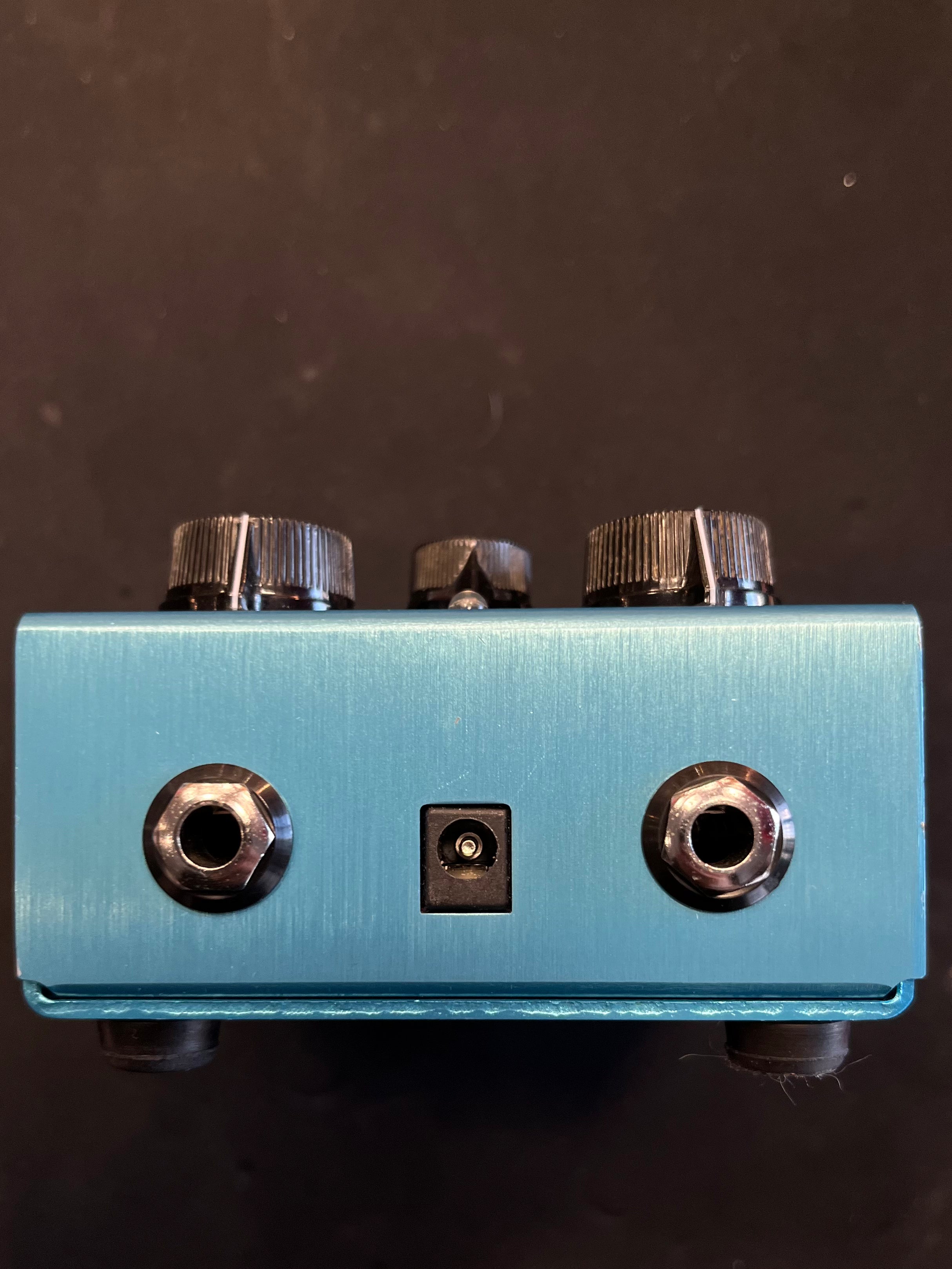 Blue pre-owned guitar effects pedal showing two audio jacks, a power input, and three black control knobs on top.