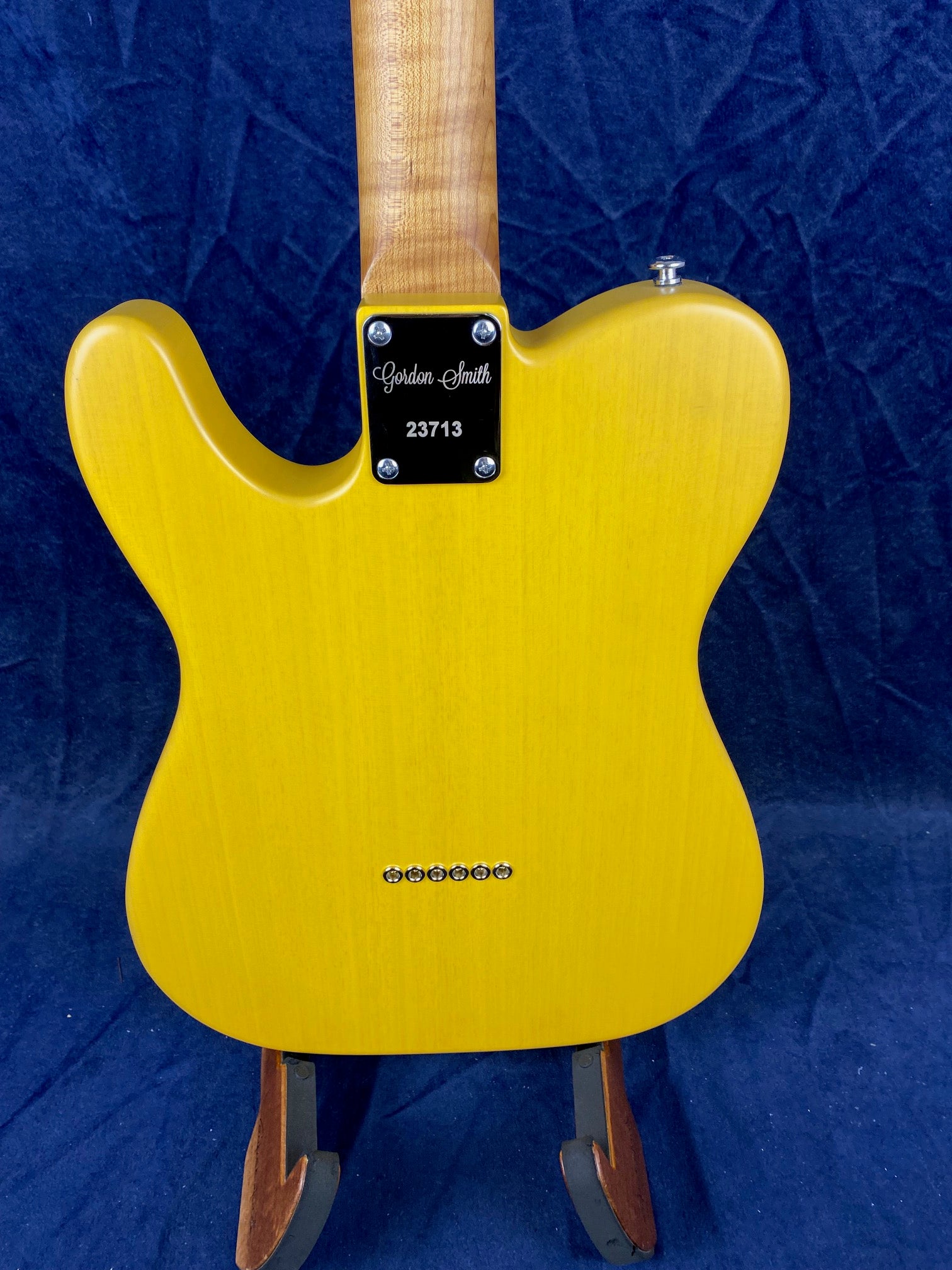 Yellow electric guitar body with a light wood neck, six string ferrules, and a neck plate labeled "Gordon Smith 23713" against a dark background.