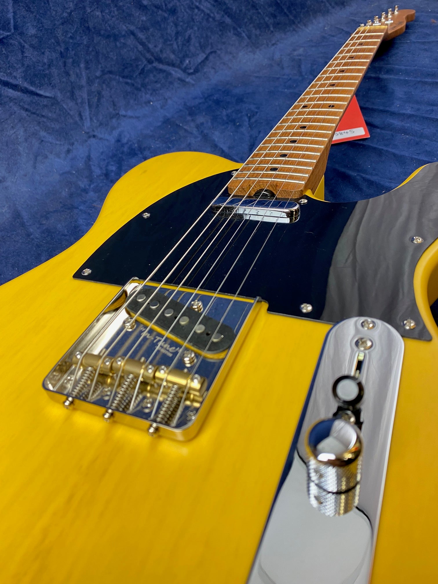 Yellow electric guitar with a black pickguard, chrome bridge, and control plate, seen from a low angle along the neck and strings.