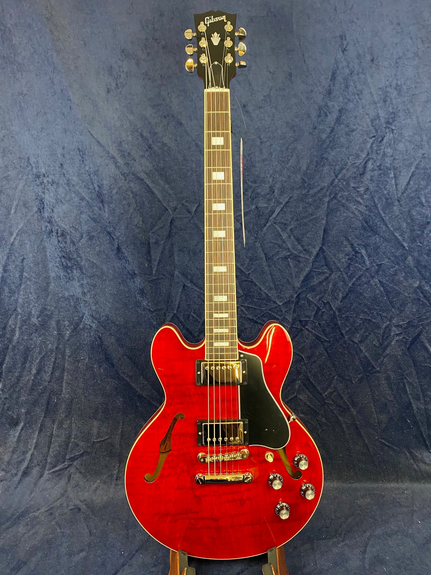 Gibson electric guitar, cherry red semi-hollow body, two humbucker pickups, black pickguard, chrome hardware, four control knobs, f-hole on left.