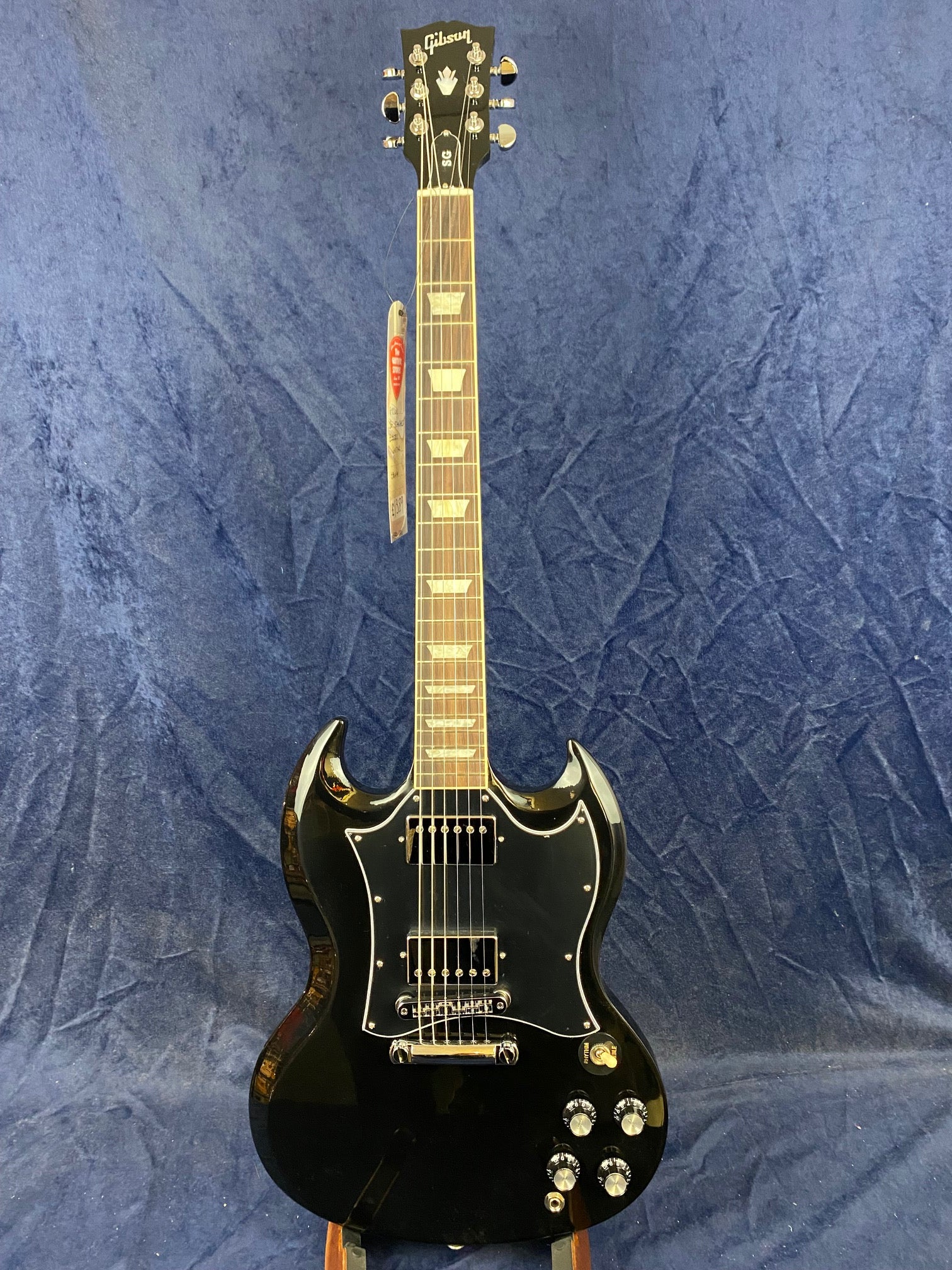 Black Gibson electric guitar with double cutaway body, chrome hardware, two humbucker pickups, and four control knobs against a blue textured background.
