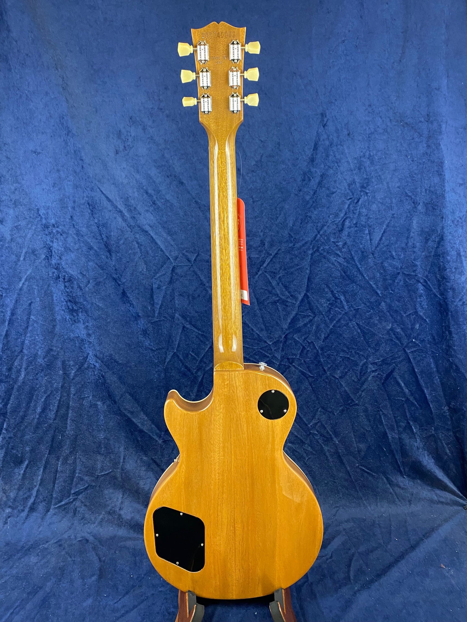 Electric guitar shown from the back, natural wood finish, two black plastic plates on the body, six tuning pegs visible on the headstock.