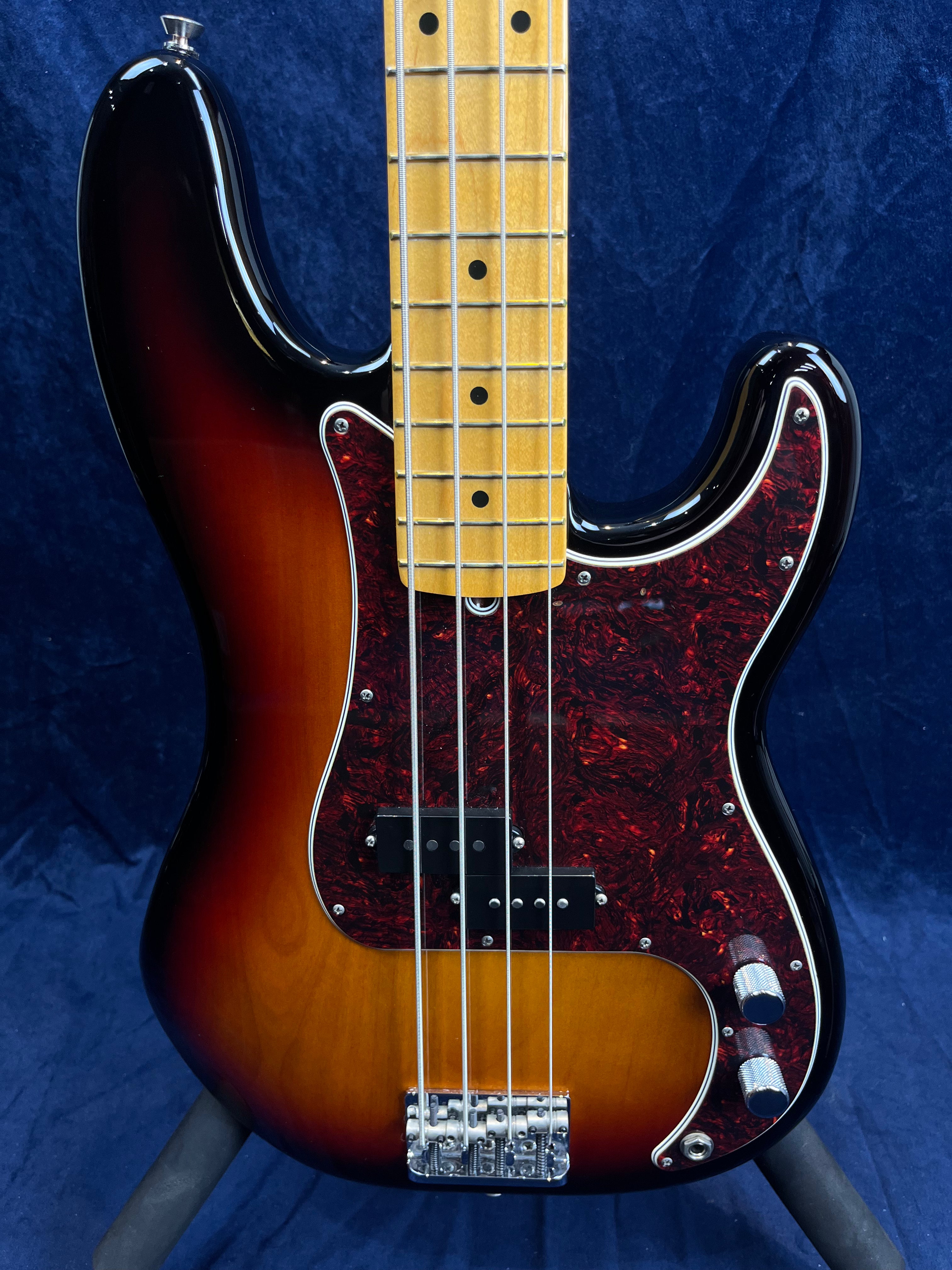 Sunburst finish bass guitar with a maple fretboard, black pickguard with red pattern, four strings, two control knobs, and chrome bridge hardware.