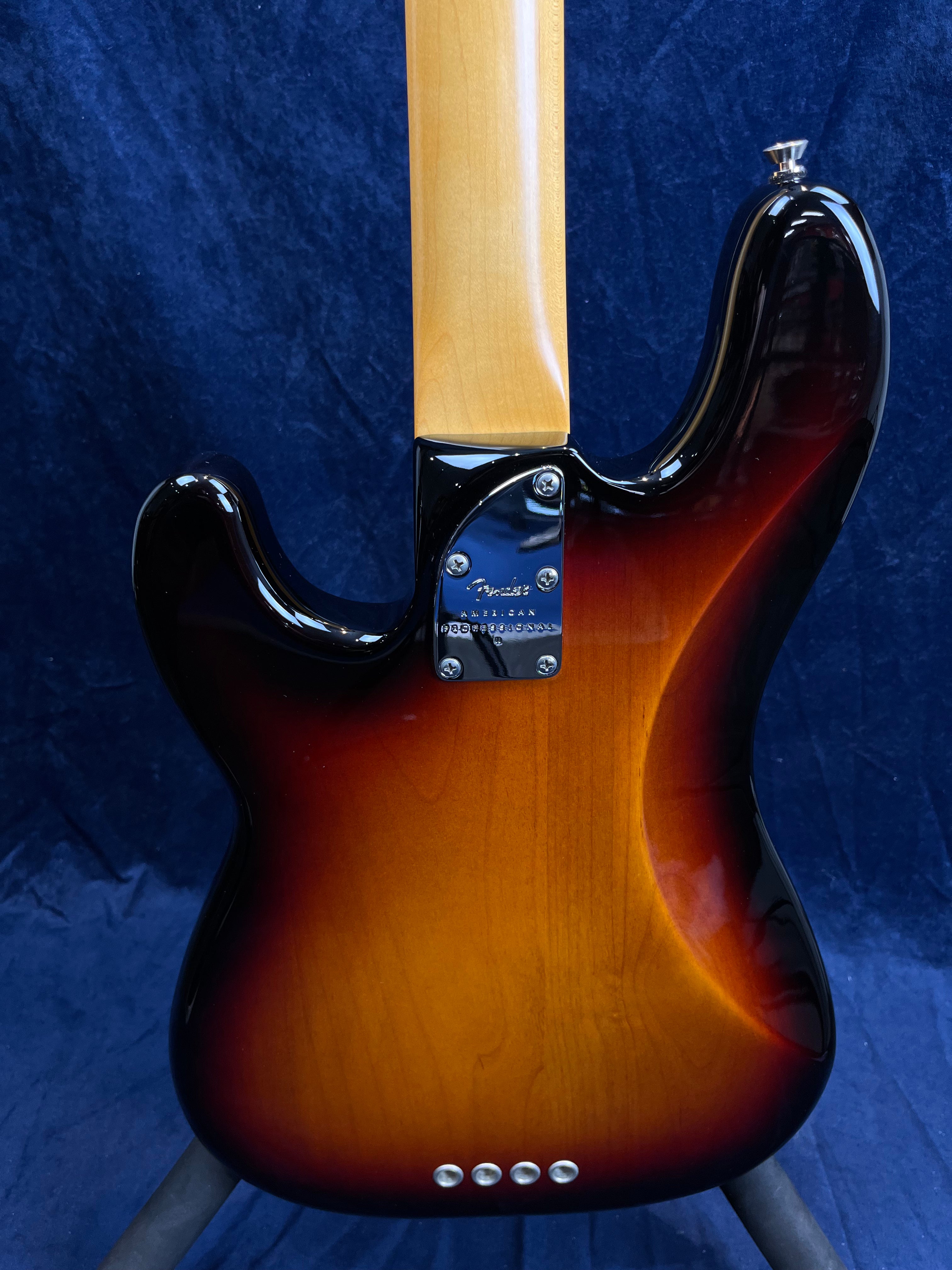 Sunburst finish bass guitar photographed from the back, with a natural wood neck and four screws attaching the neck plate to the body.