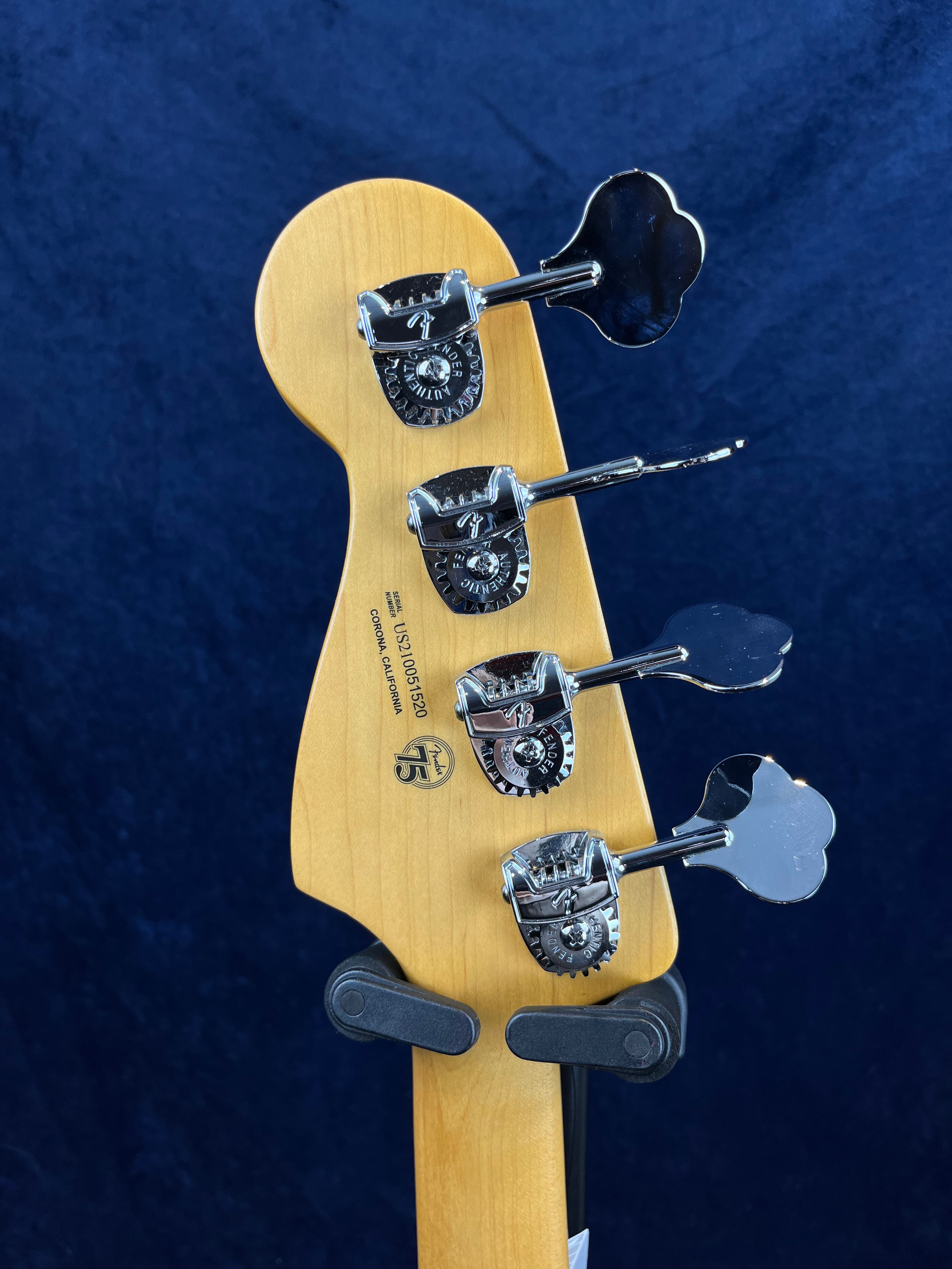 Back of a bass guitar headstock showing four chrome tuning pegs, a natural wood finish, and a Fender 75th anniversary logo.