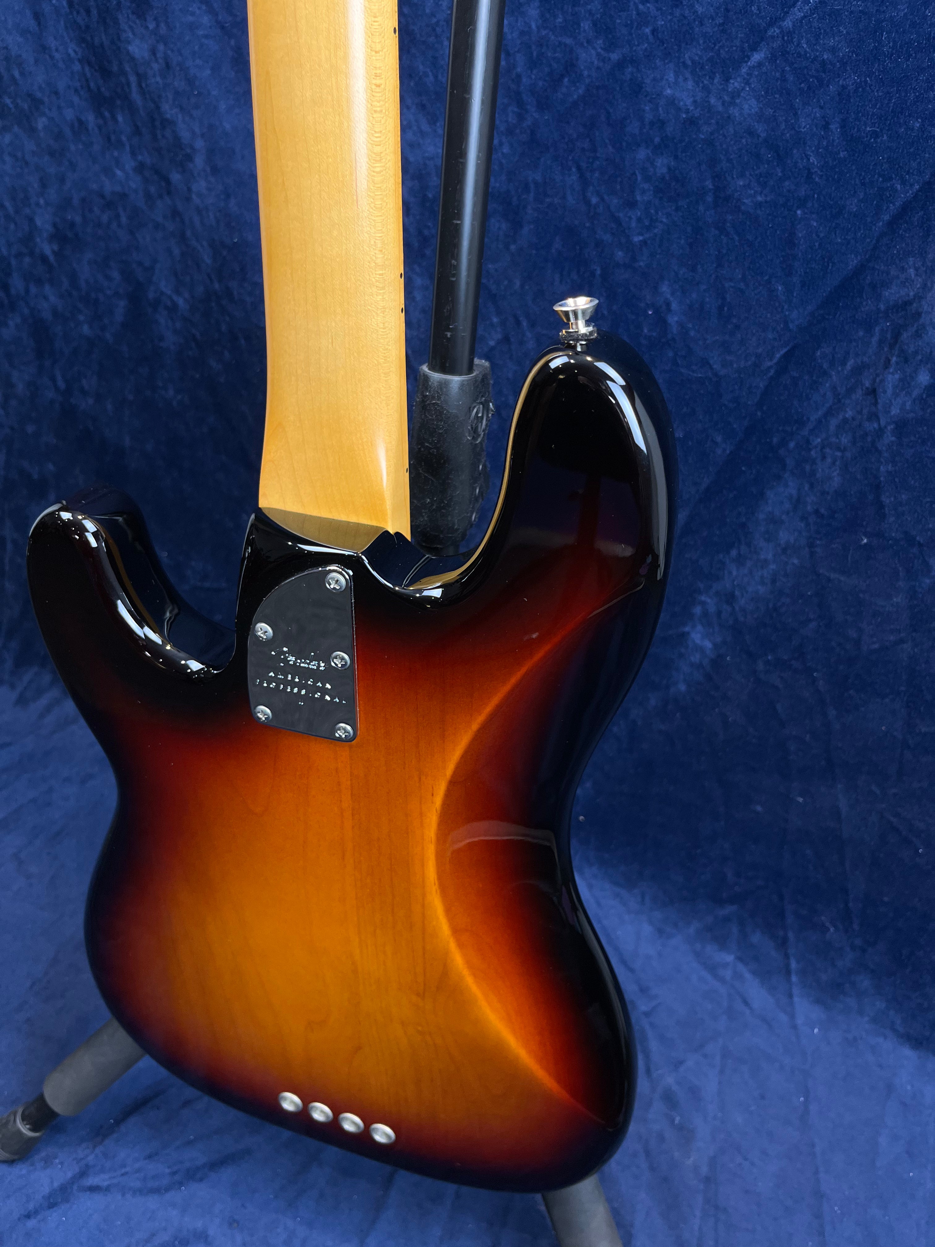 Sunburst finish bass guitar shown from the back on a stand, highlighting its glossy wood grain and four-bolt neck plate.