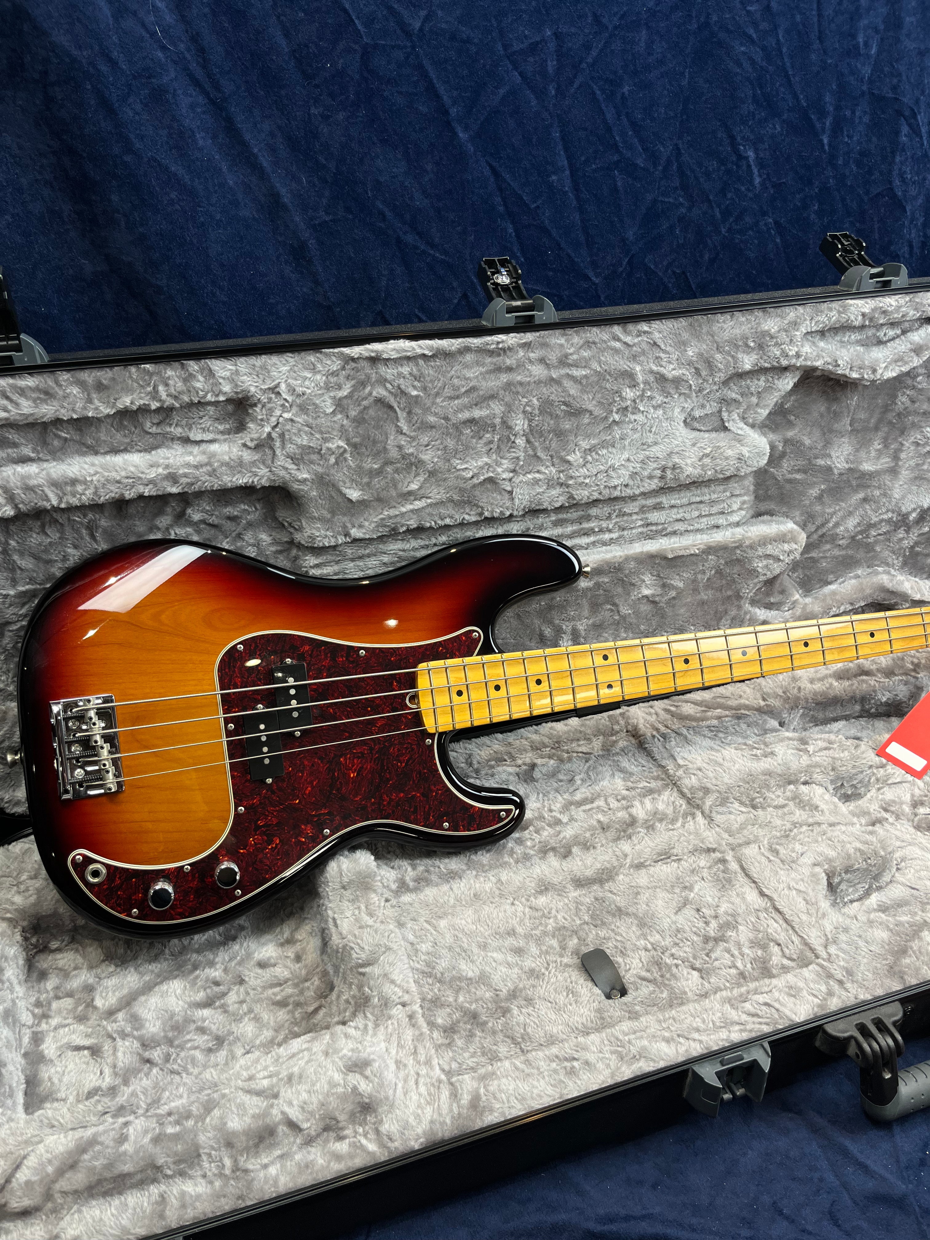 Sunburst finish bass guitar with a maple neck and tortoiseshell pickguard rests in a gray plush-lined hard case.