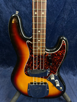 Sunburst finish bass guitar with four strings, rosewood fretboard, red tortoiseshell pickguard, and chrome covers over pickups and bridge.