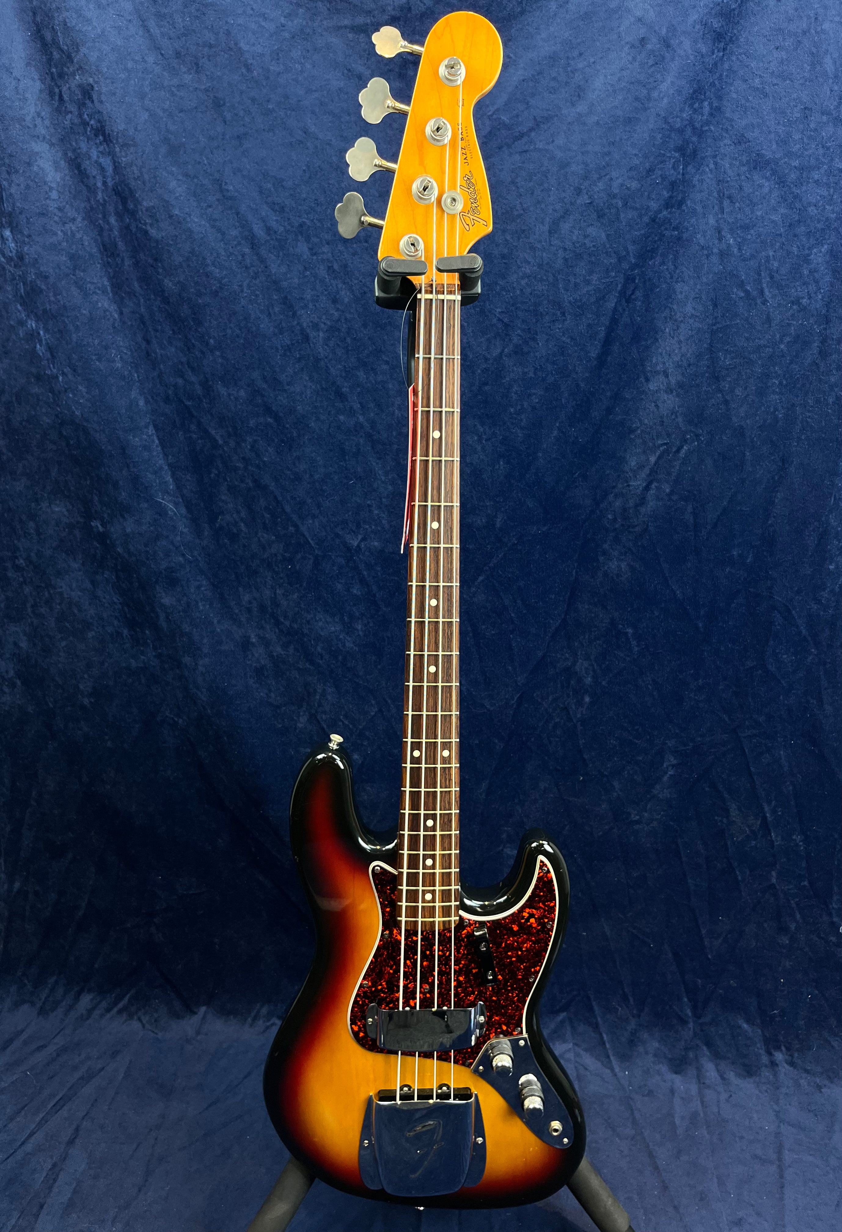Sunburst Fender Jazz Bass guitar with a dark red tortoiseshell pickguard, chrome pickup covers, and four tuning pegs on a light maple headstock.