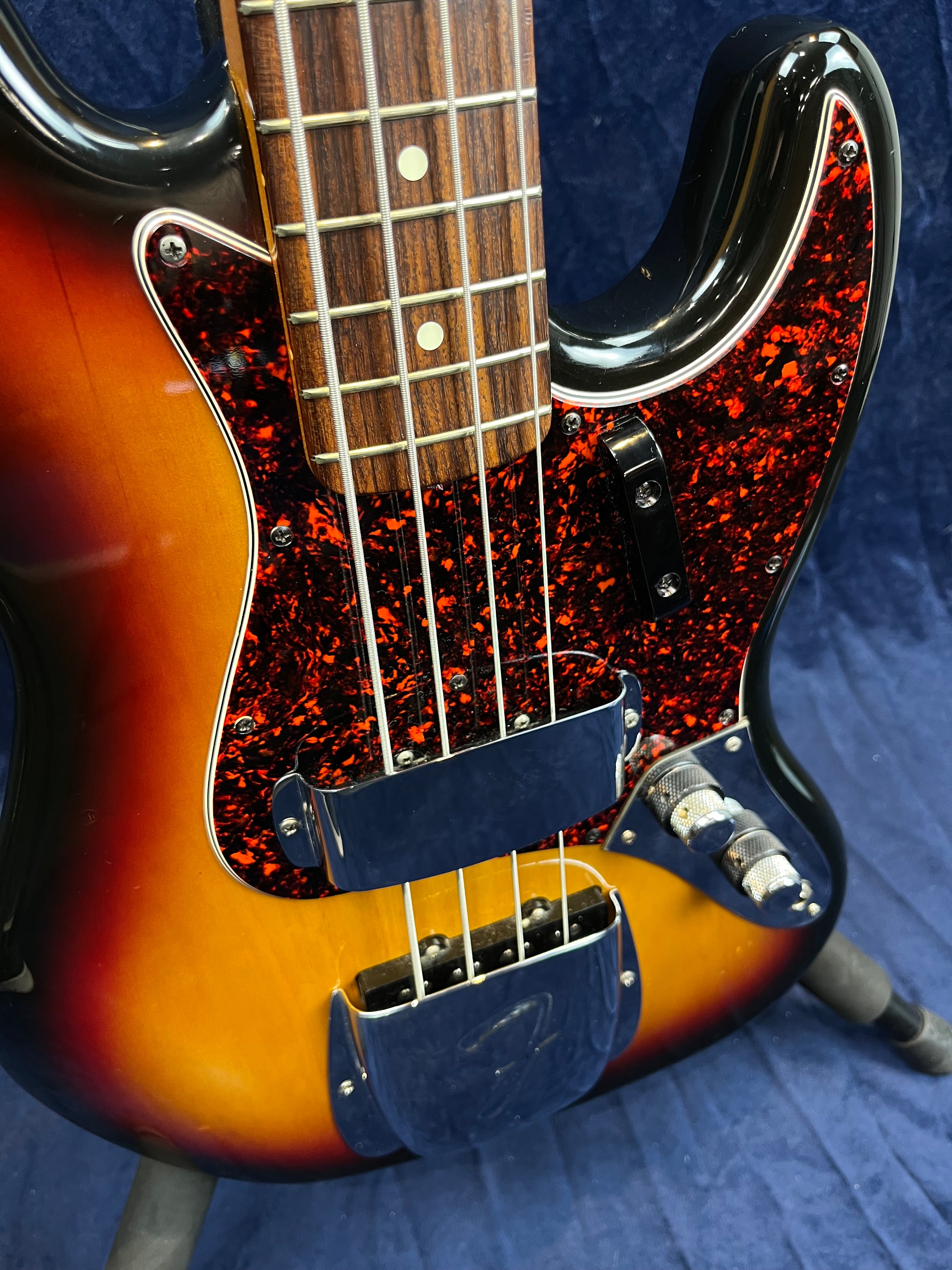 Sunburst finish bass guitar with a red tortoiseshell pickguard, chrome pickup and bridge covers, and a rosewood fingerboard with dot inlays.