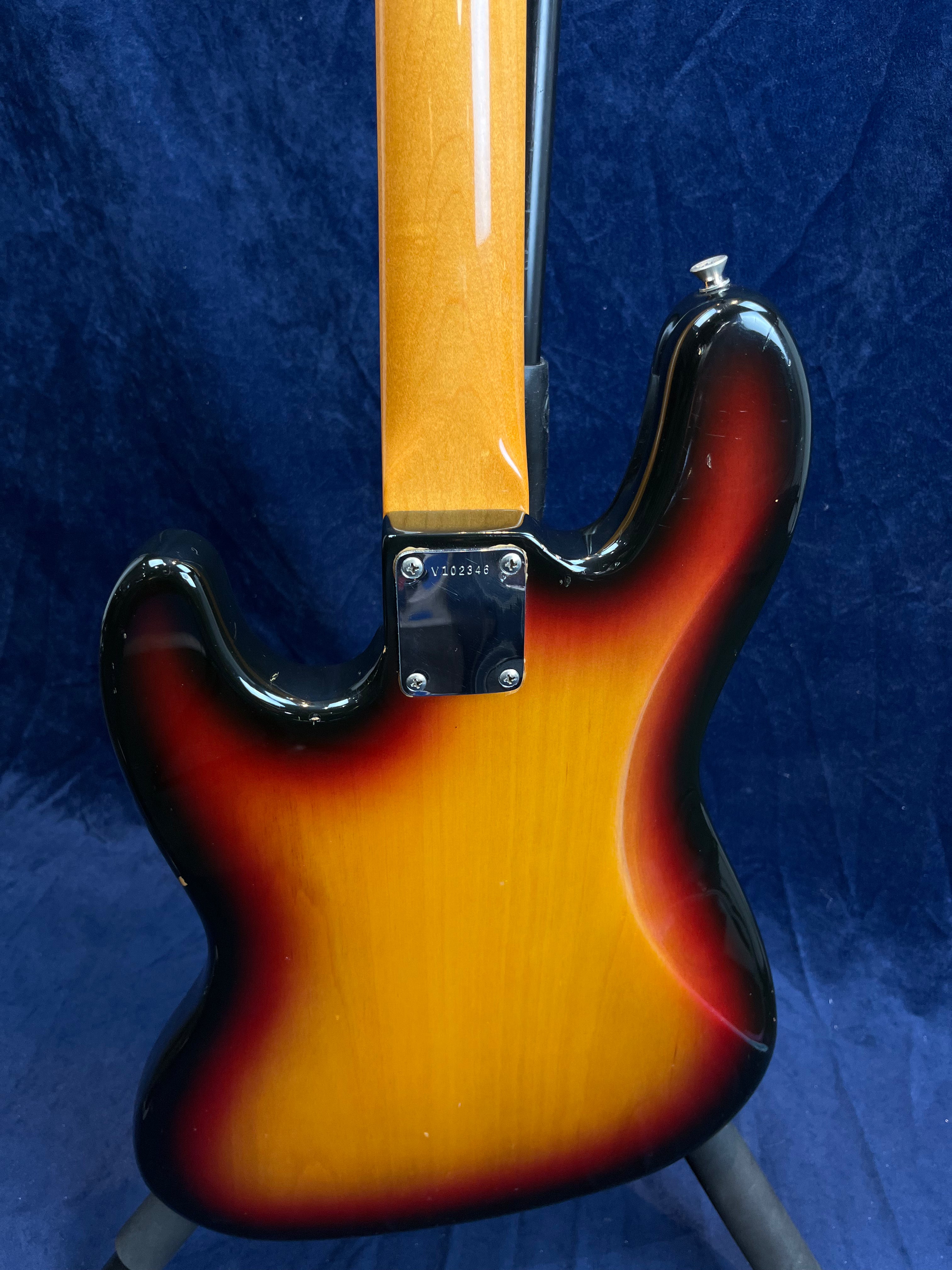 Sunburst-finish bass guitar shown from the back, highlighting the screw plate, neck joint, and contoured wooden body against a blue background.