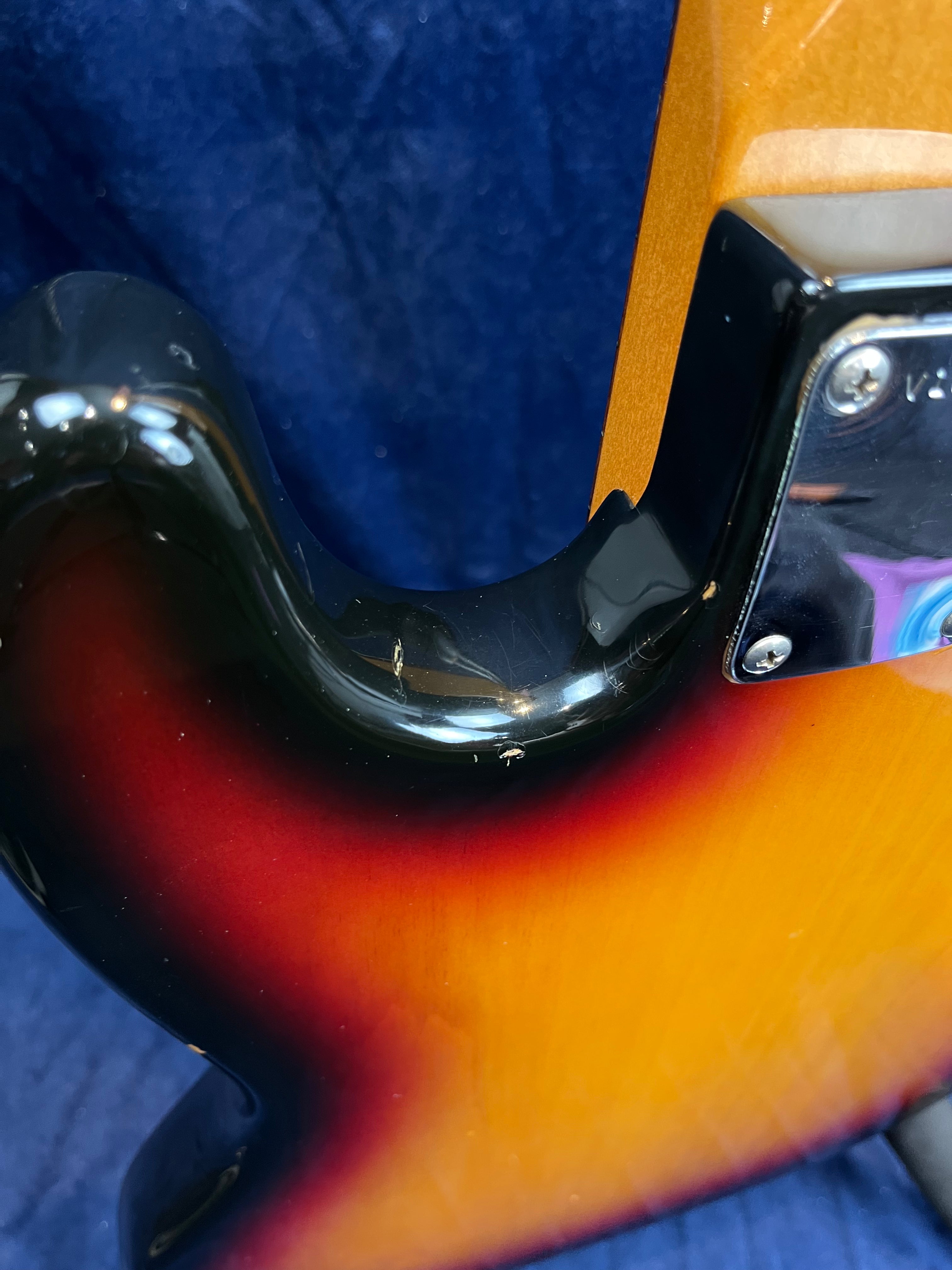Close-up of a sunburst bass guitar body showing minor chips and scratches near the neck joint where the black and yellow paint meet.
