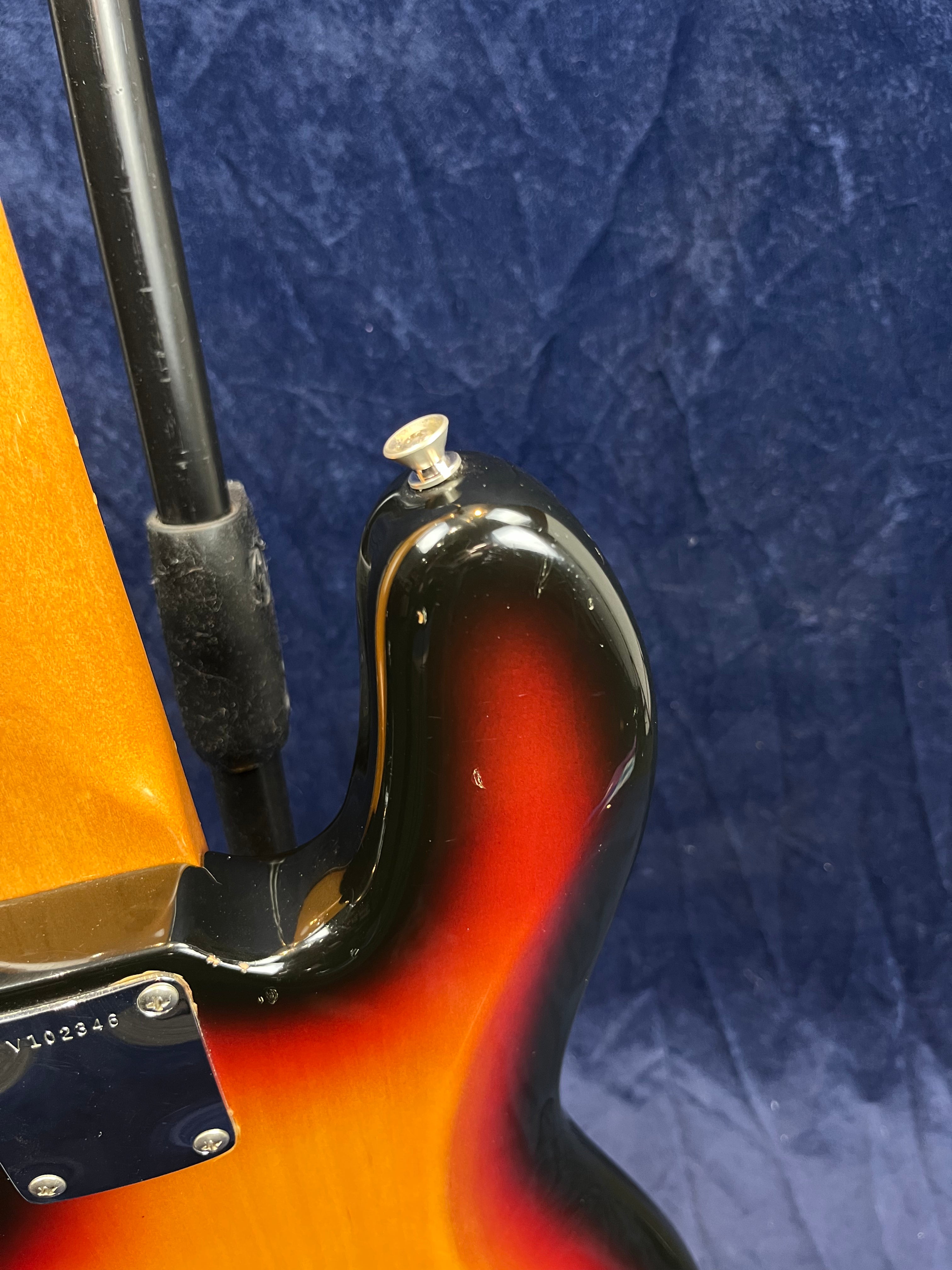 Sunburst-finish bass guitar body close-up shows the neck joint, strap button, and some light scratches on the glossy surface.