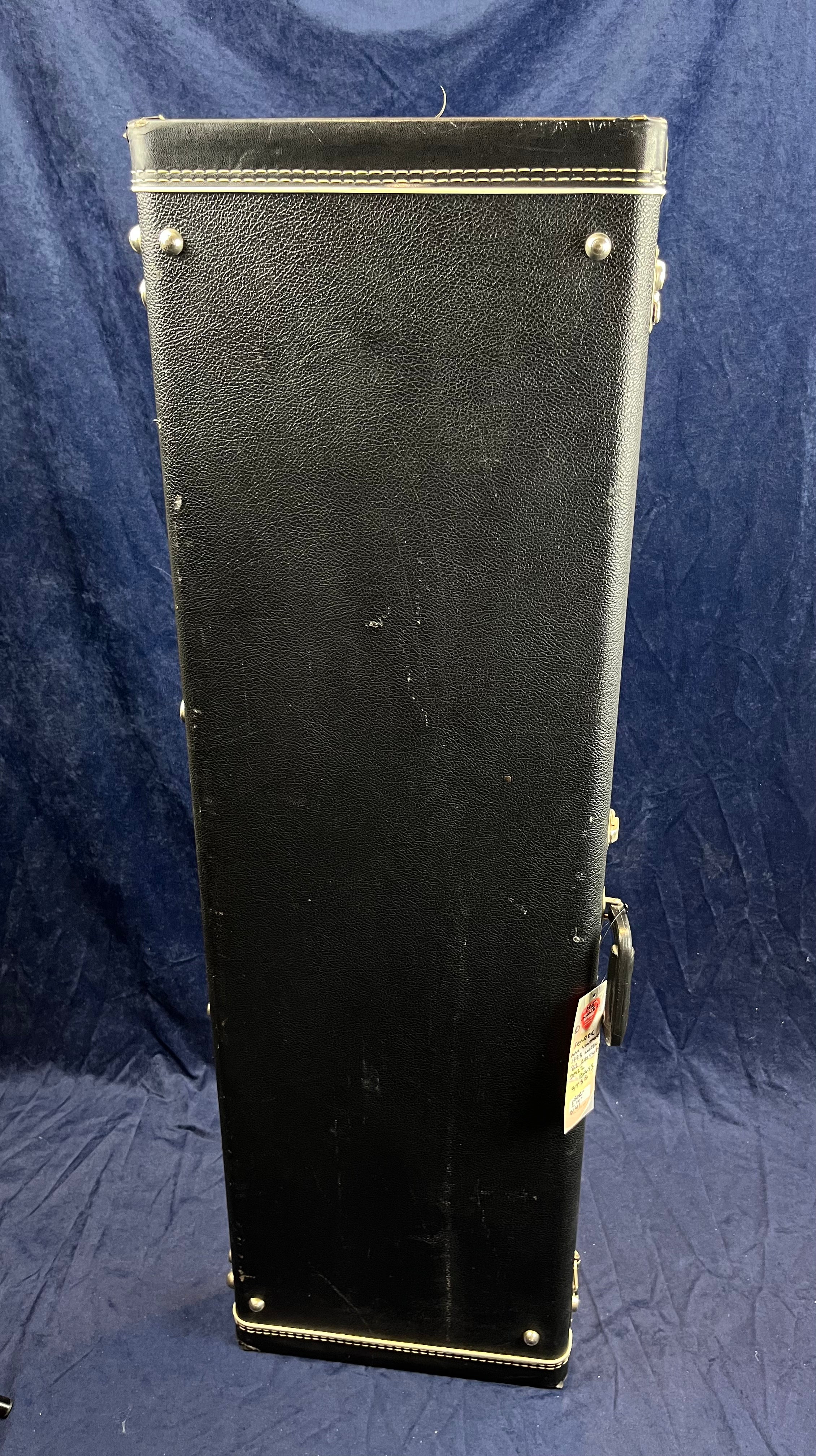 Tall, rectangular hard case for bass guitar in black with metal corner studs, white stitching near edges, and a handle on the right side.