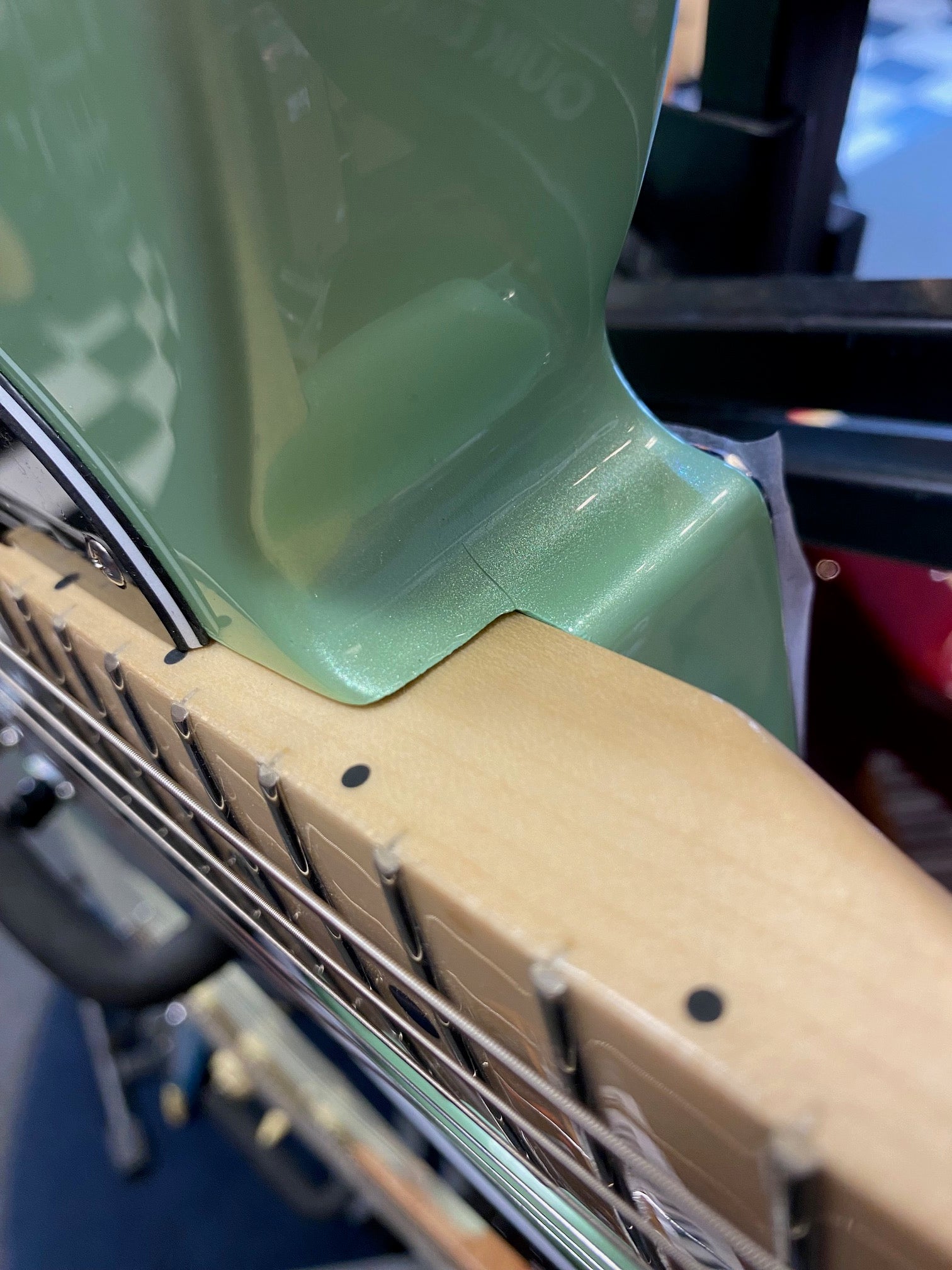 Close-up of a green electric guitar’s neck joint, showing the maple fretboard, metal frets, and glossy body finish.