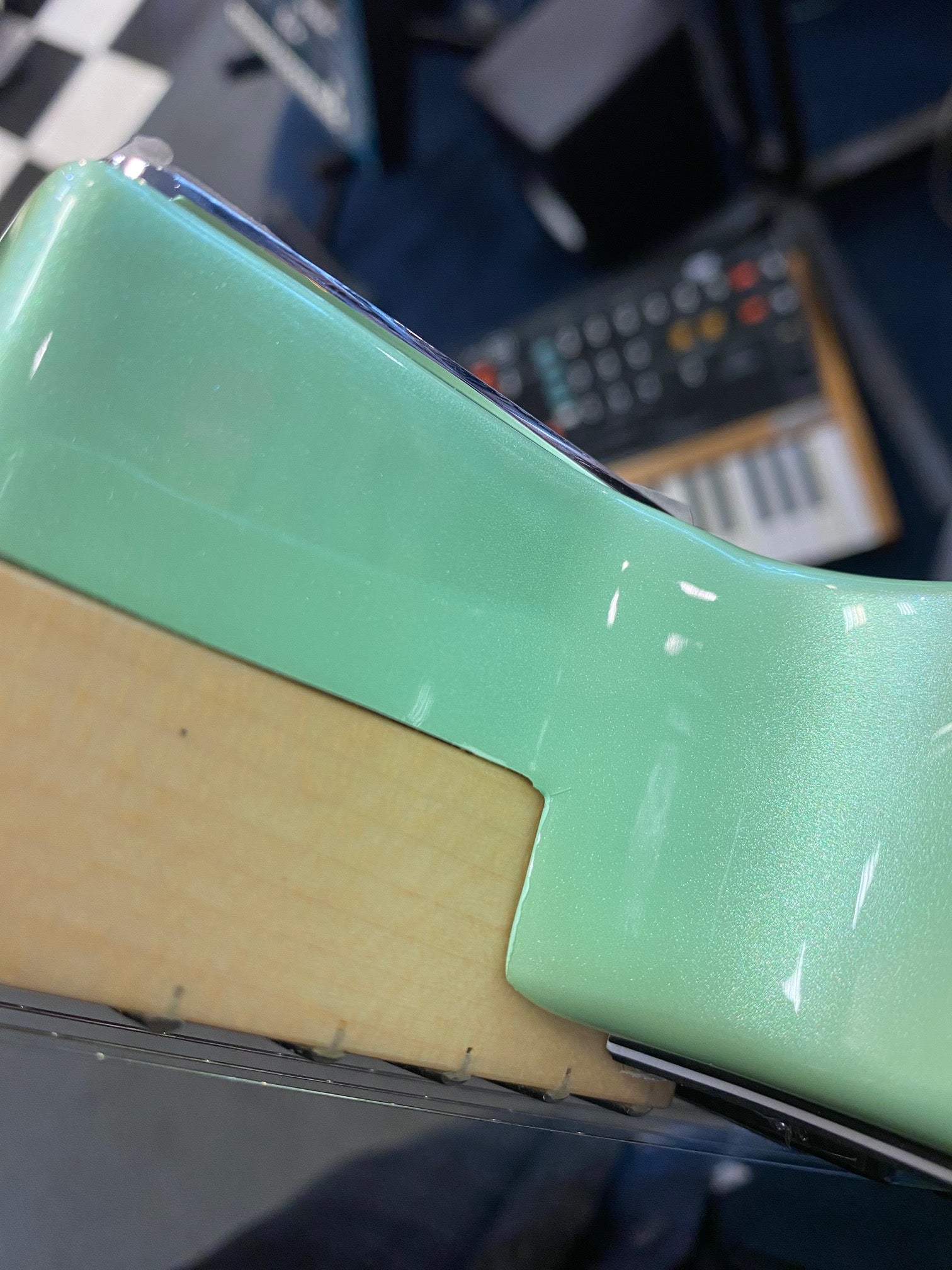 Close-up of an electric guitar neck joint showing a mint green glossy body finish meeting a natural maple neck.