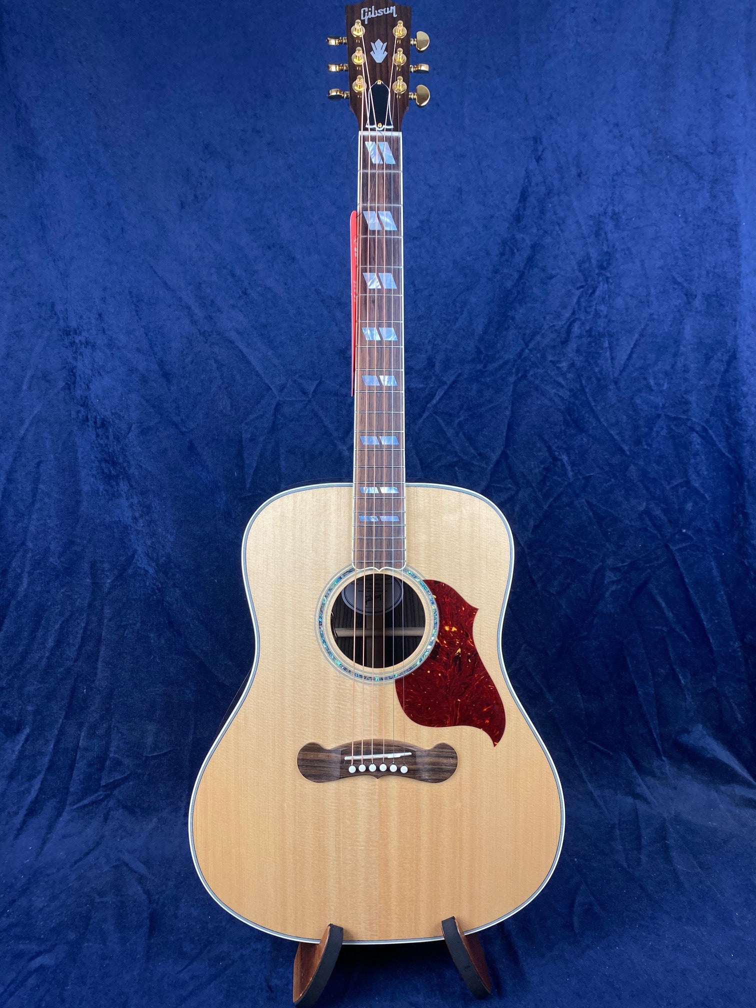 Natural-finish Gibson acoustic guitar with gold tuning pegs, abalone rosette, rectangular fret inlays, and a red tortoiseshell pickguard.