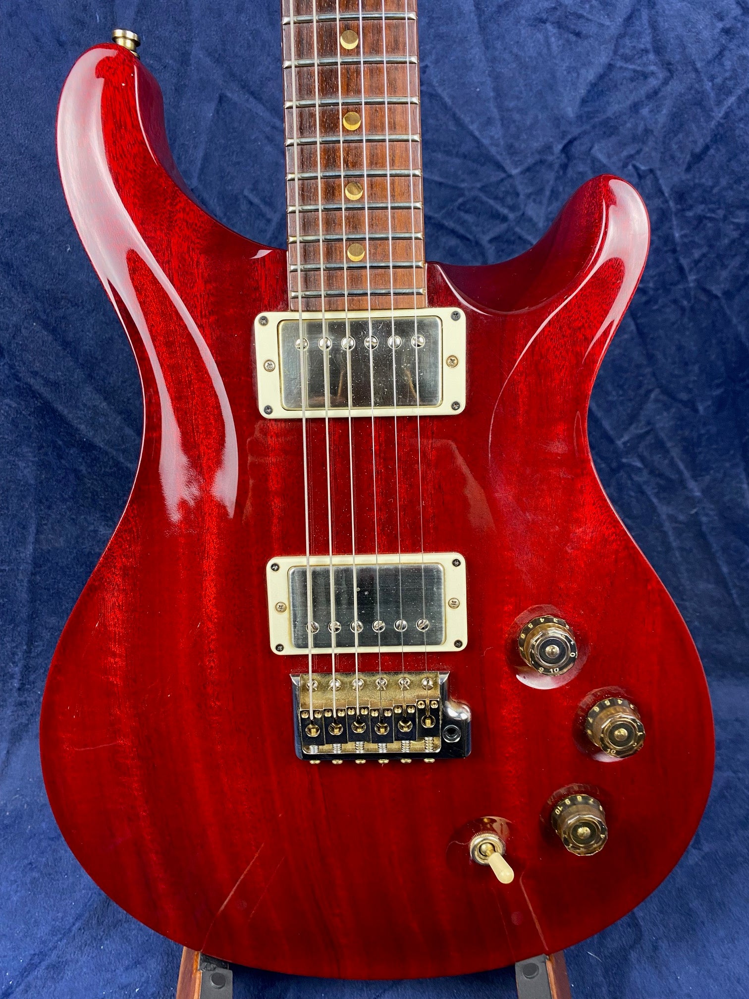 Deep red electric guitar with two chrome humbucker pickups, three gold control knobs, a toggle switch, and a rosewood fretboard with dot inlays.