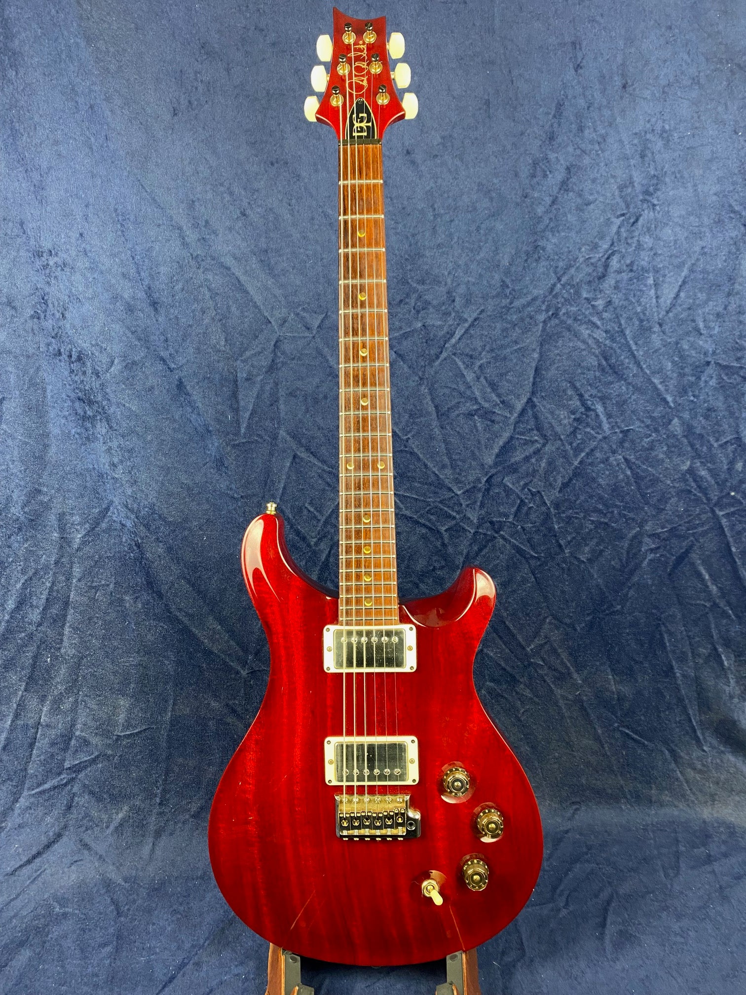 Glossy red double-cutaway electric guitar with two humbucker pickups, three knobs, and a switch, displayed against a dark blue textured background.