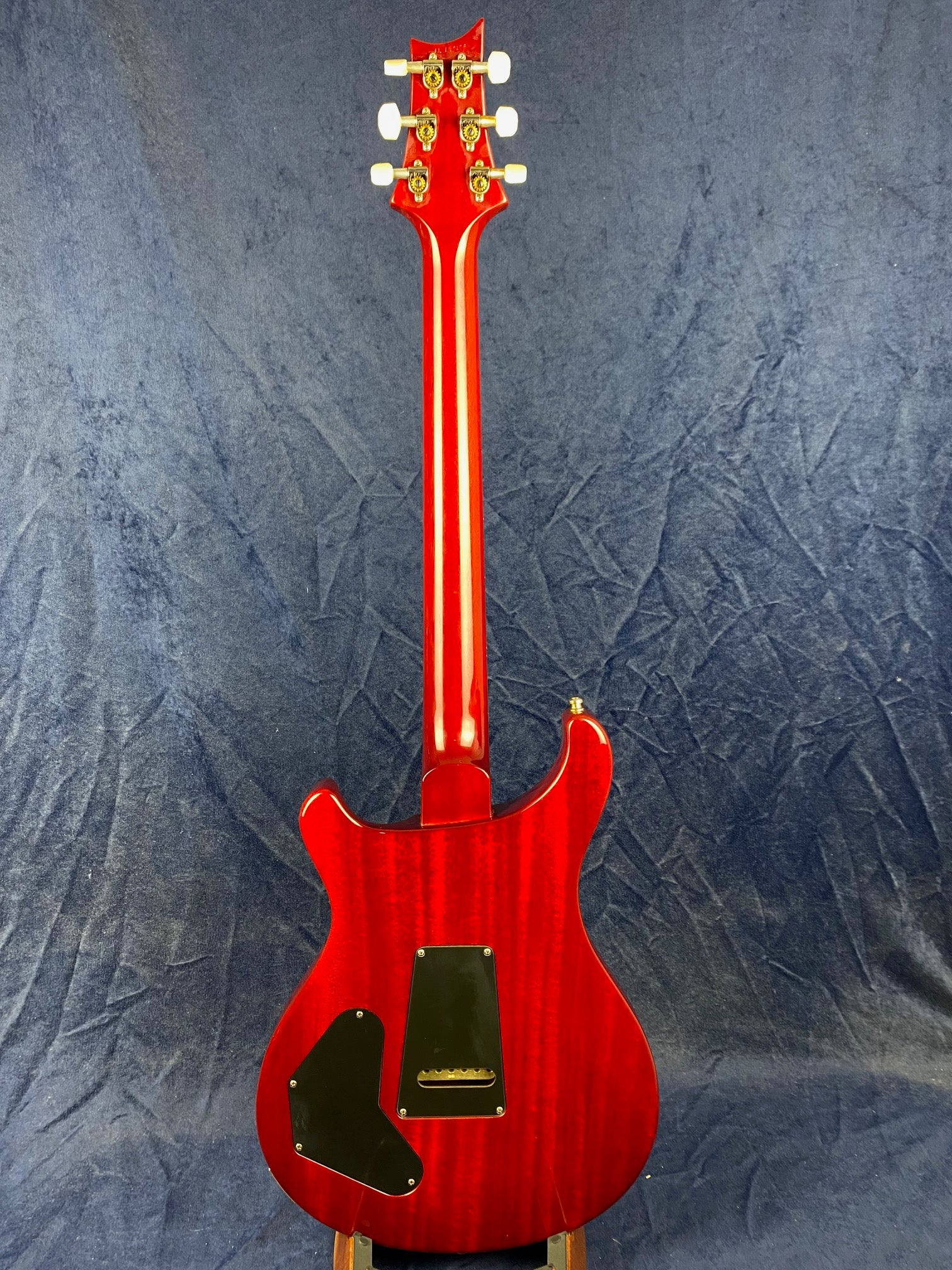Red electric guitar shown from the back, revealing gold tuning pegs, two black electronic cavity covers, and a glossy wood finish.