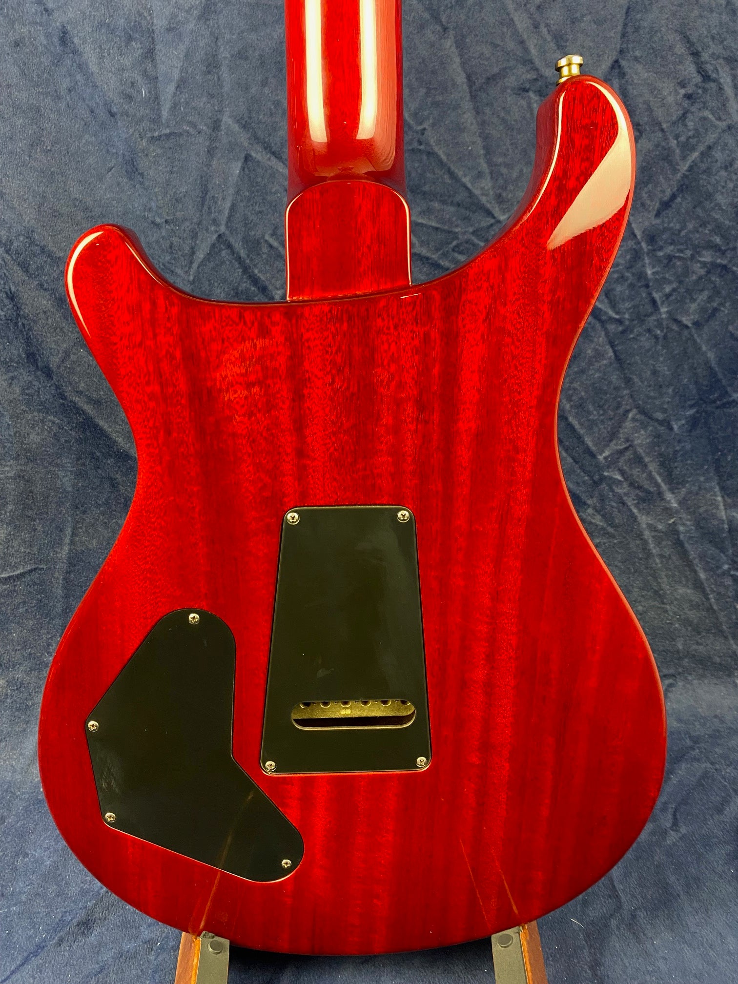 Glossy red electric guitar back with two black plastic access covers and a dark blue textured background.