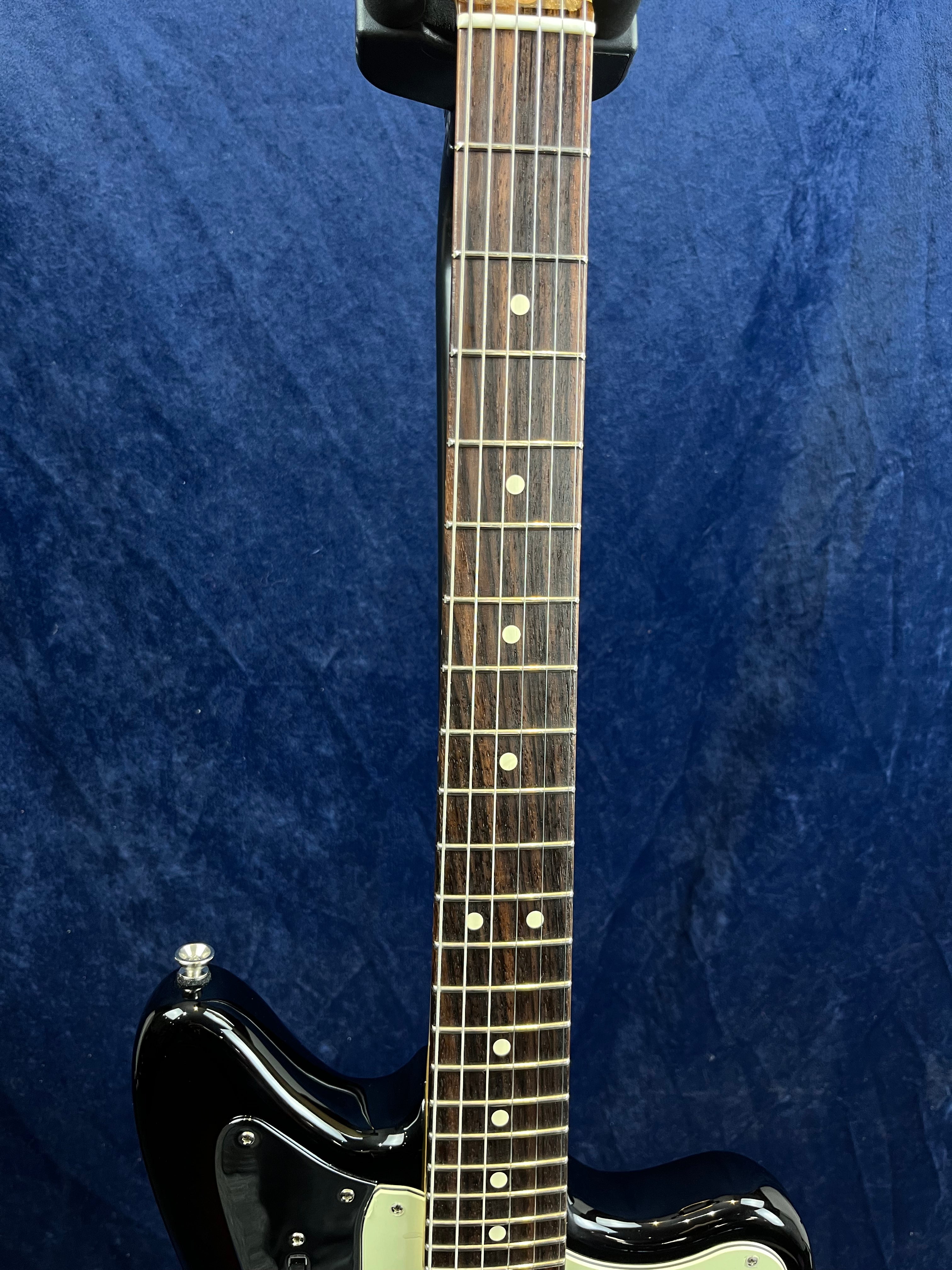 A black electric guitar with a rosewood fretboard and dot inlays, shown upright against a dark blue textured background.