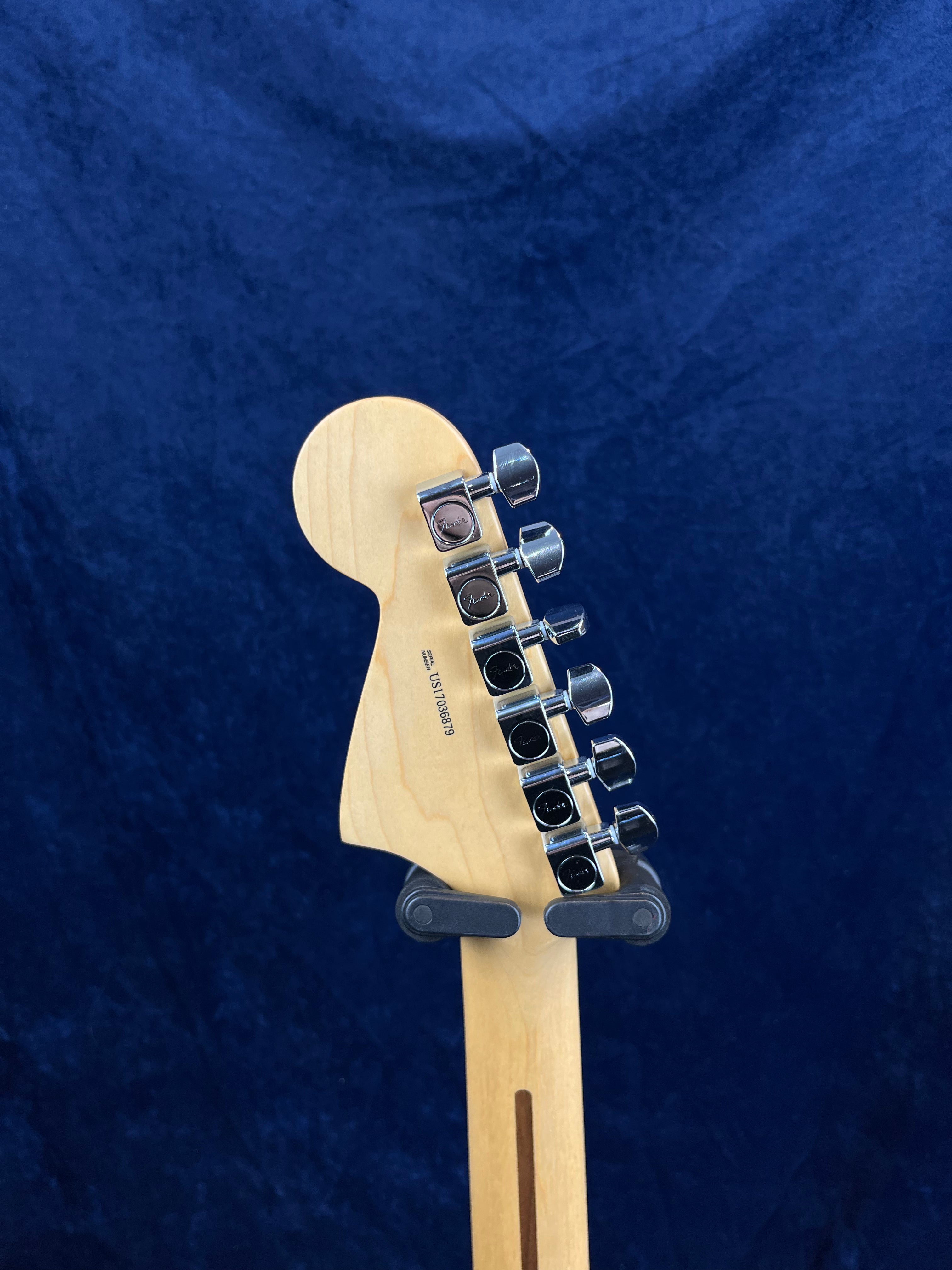 Six tuning pegs line the back of a natural wood electric guitar headstock, set against a dark blue background.
