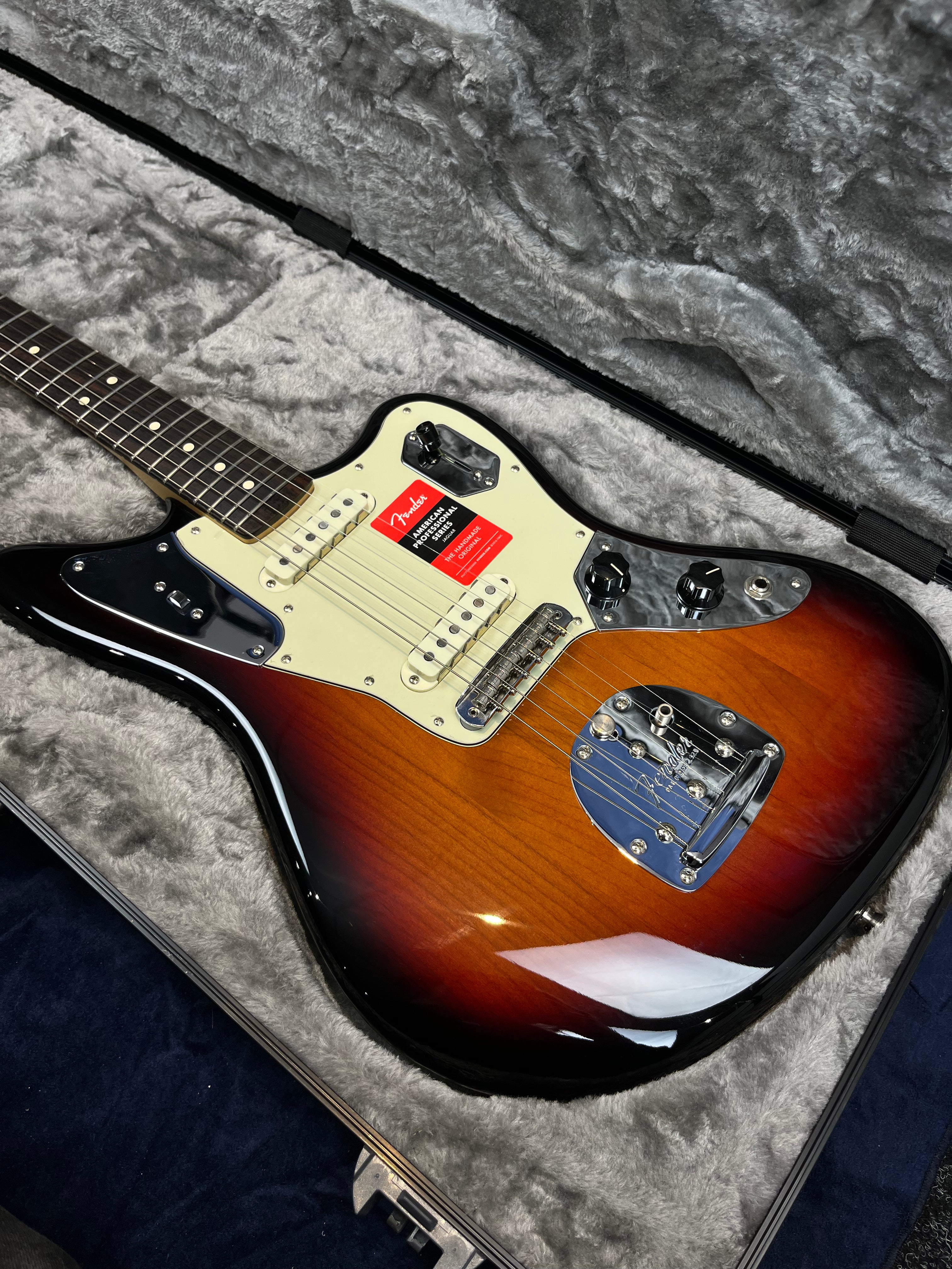 Sunburst Fender electric guitar with white pickguard and chrome hardware, resting in a gray plush-lined hard case.