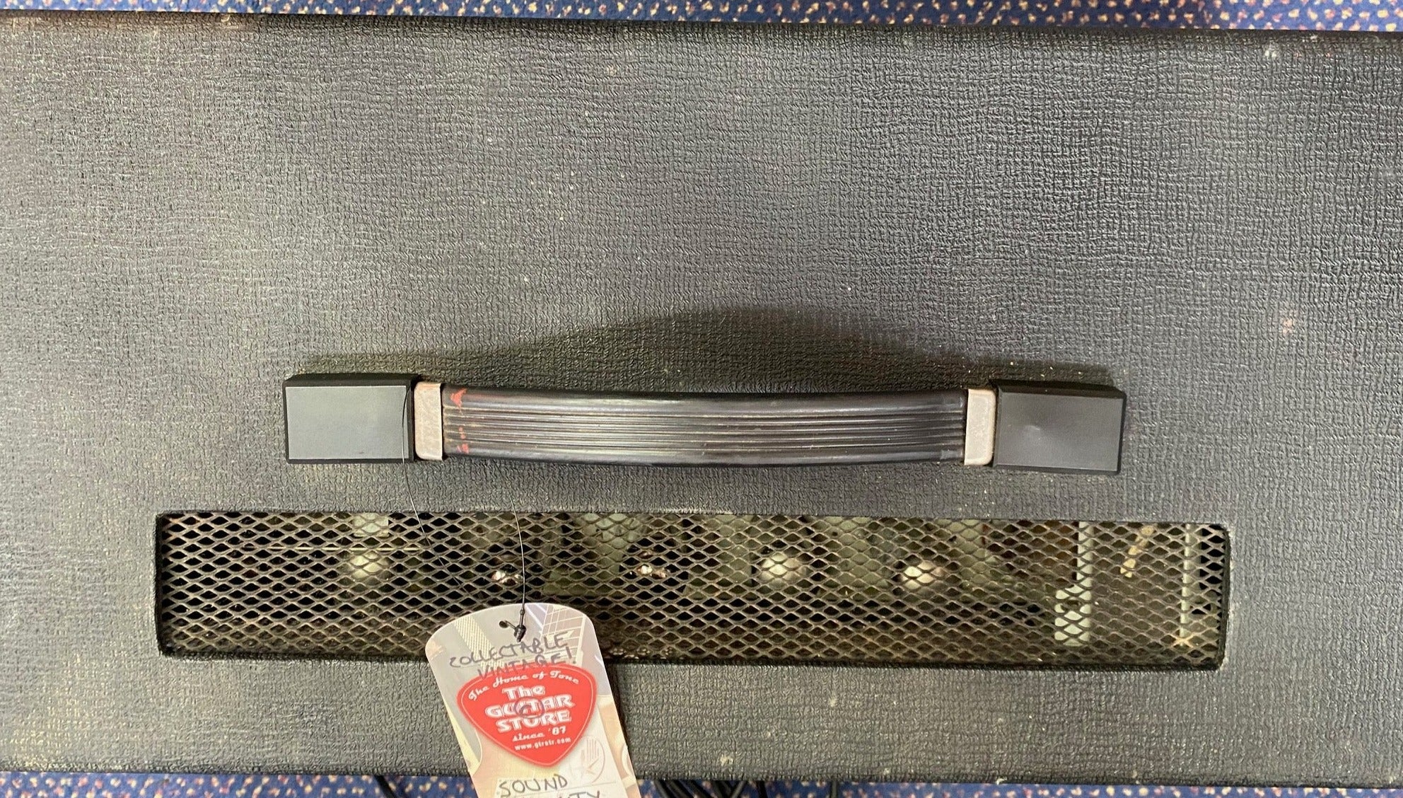 Black guitar amplifier with a textured surface, a sturdy top handle, and a vented grille revealing inner tubes; a store tag is attached.