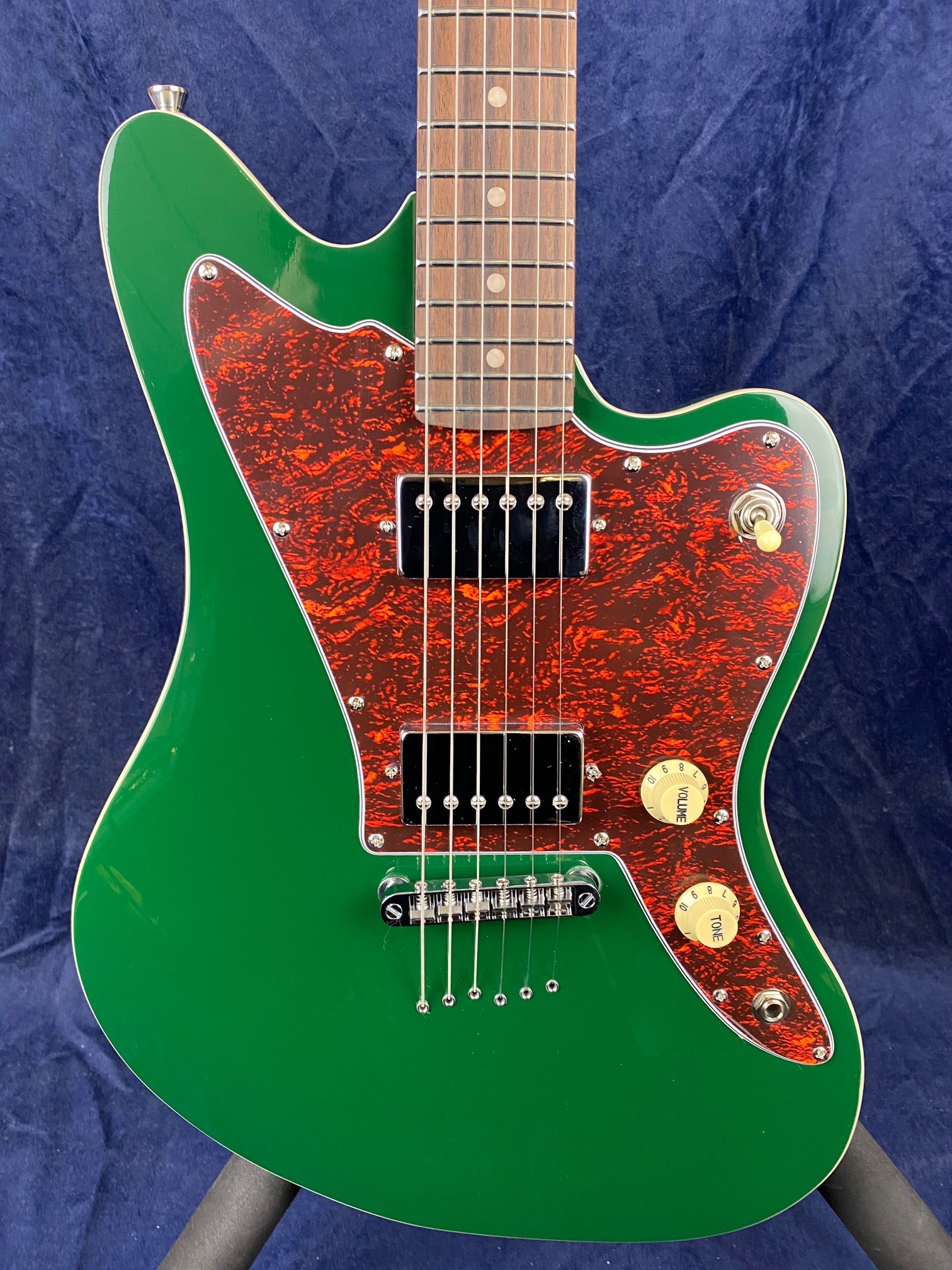 Green electric guitar with a reddish-brown pickguard, two black humbucker pickups, two cream control knobs, and a silver bridge.