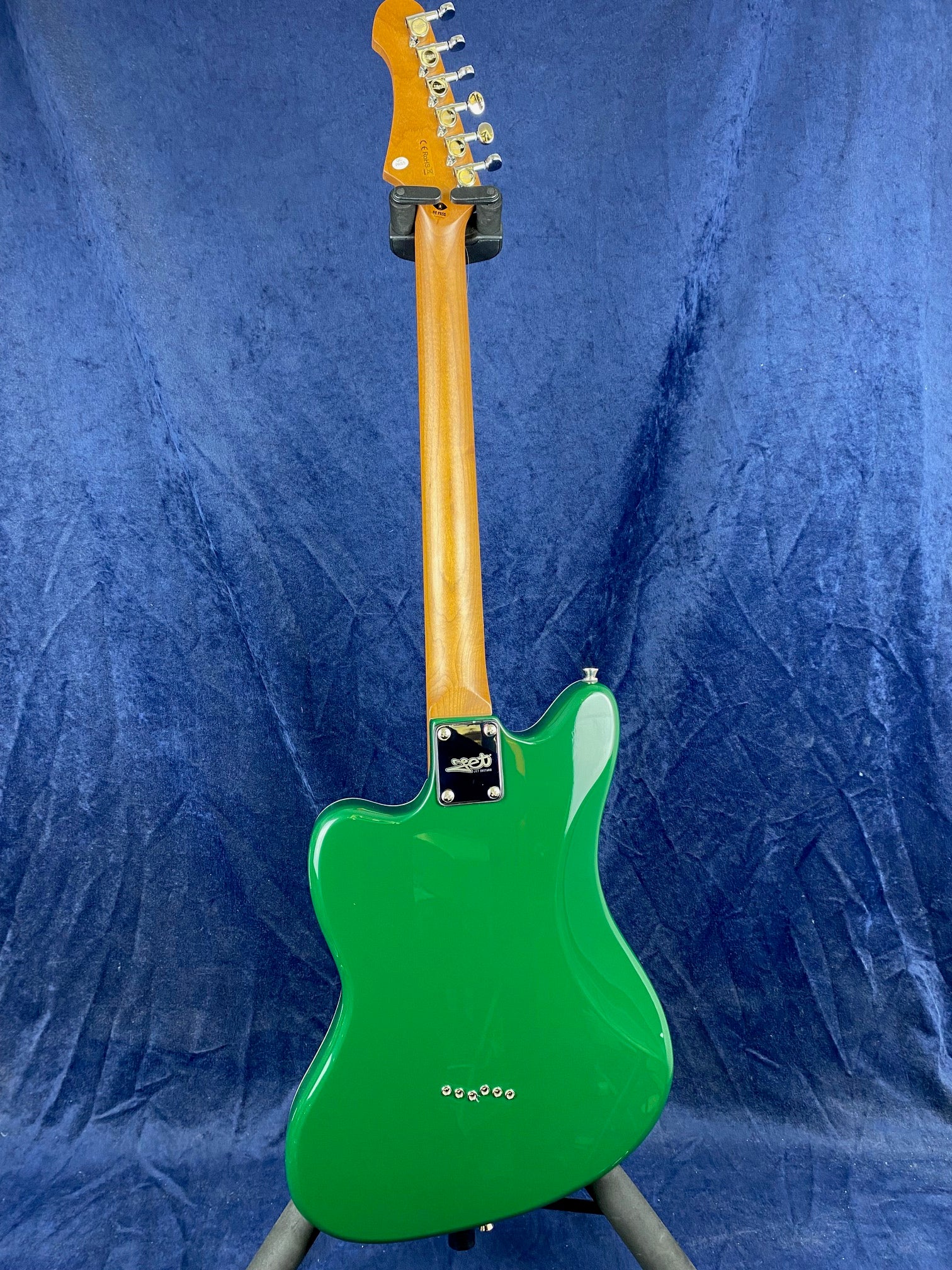 Green electric guitar shown from the back, with a natural wood neck and chrome tuning pegs against a blue background.