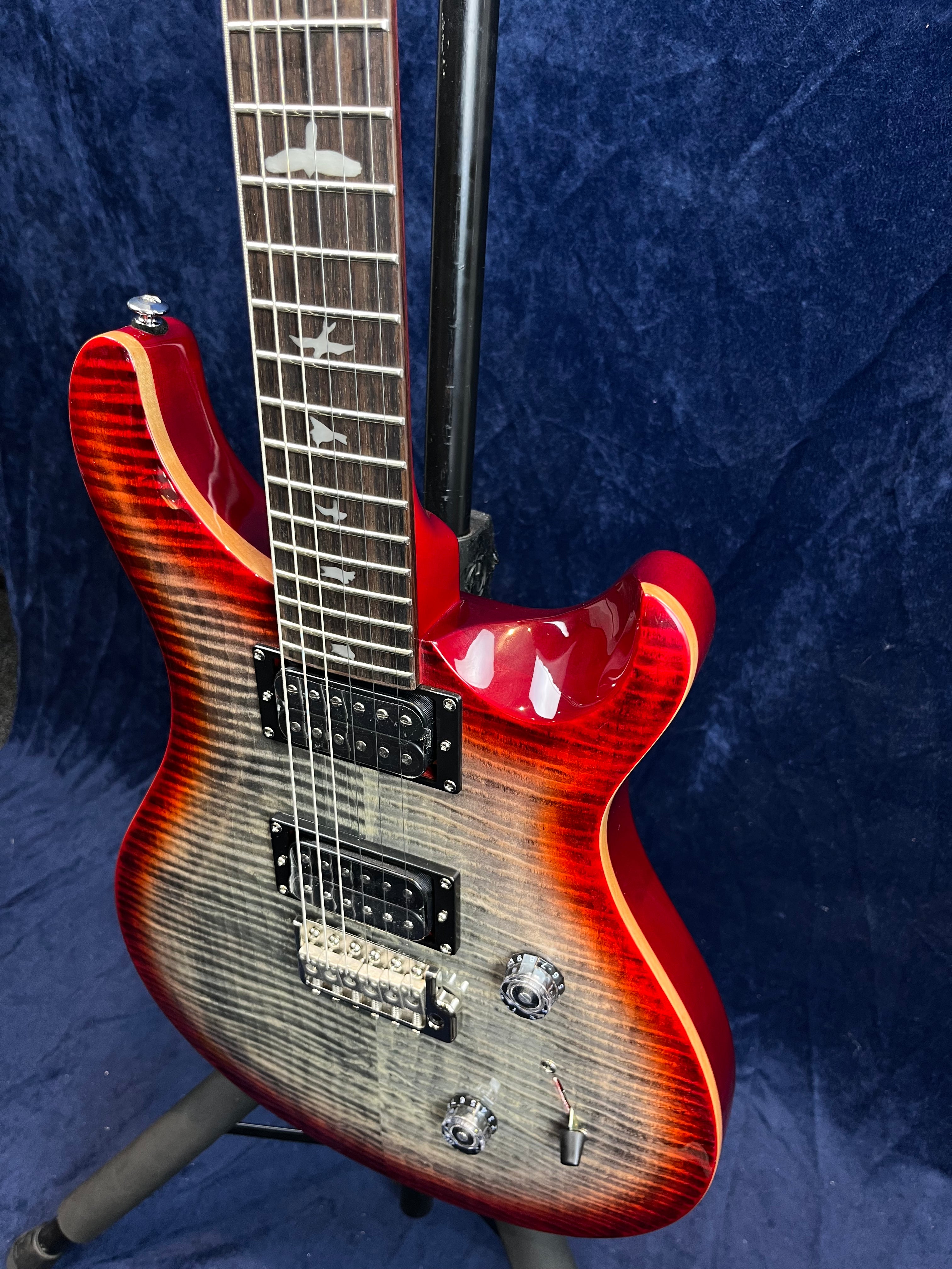 Red electric guitar with a flamed maple top, bird inlays on the fretboard, two humbucker pickups, and chrome control knobs.