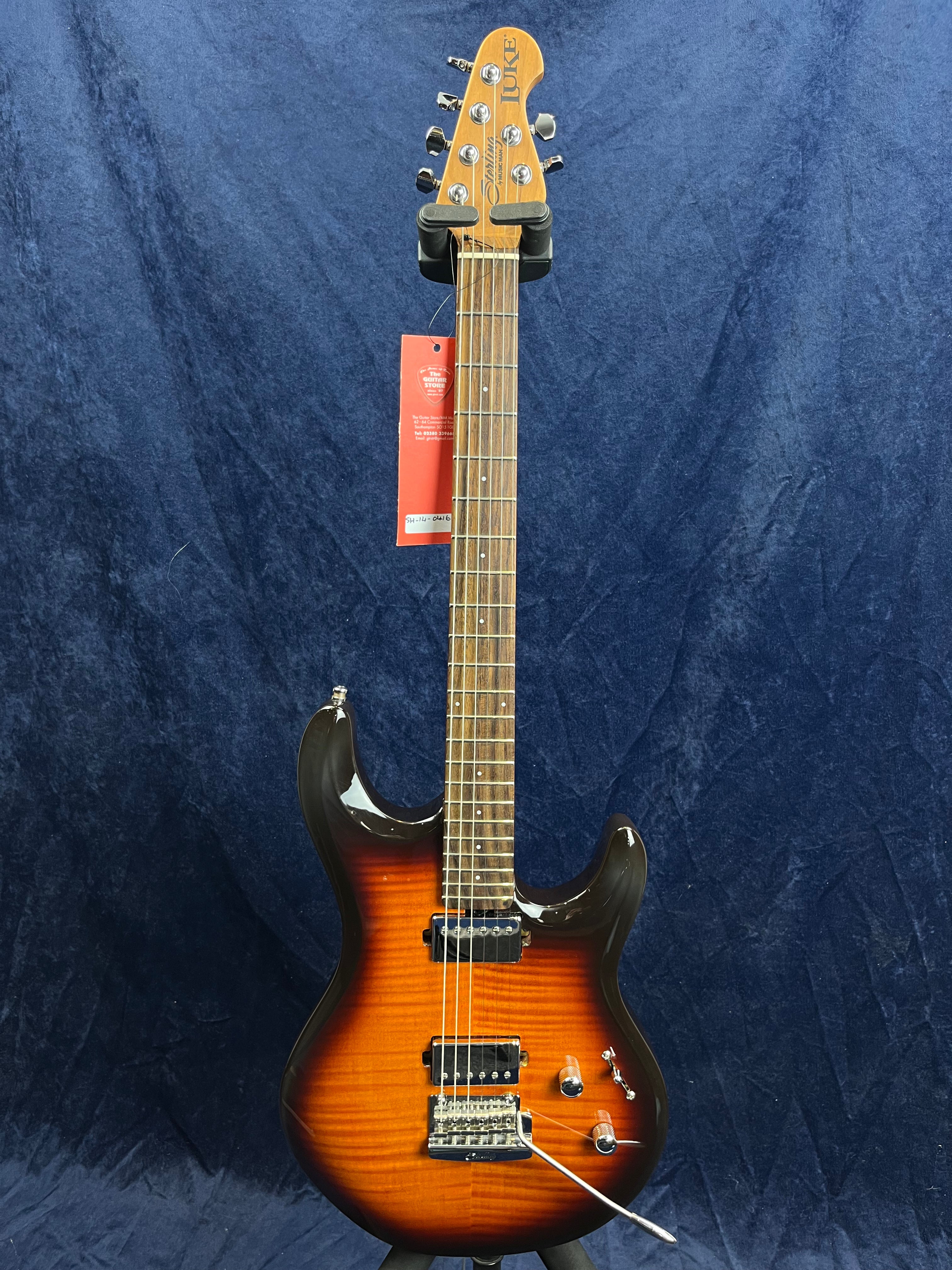 Sunburst electric guitar with two humbucker pickups, a whammy bar, and chrome hardware, displayed against a dark blue textured background.